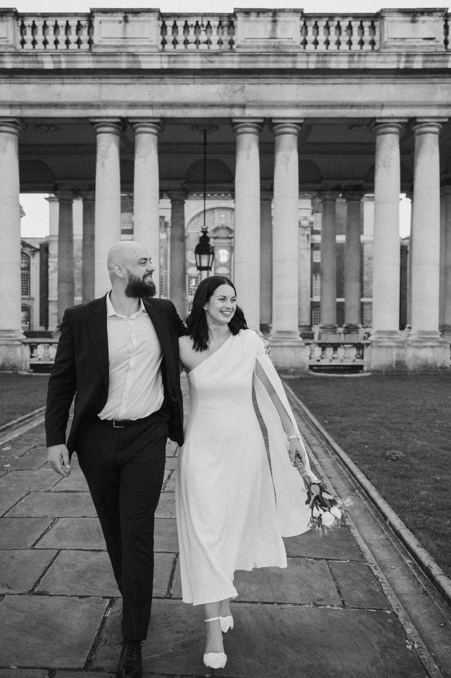 A couple strolls past classical architecture columns during their wedding photoshoot.