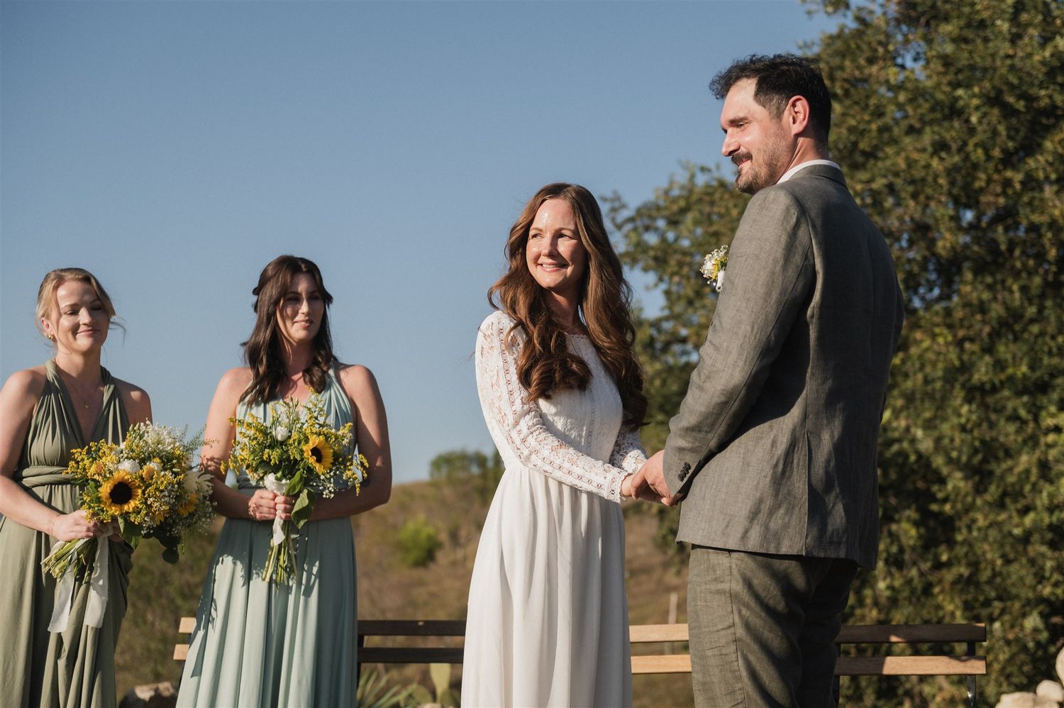 A wedding party poses outdoors against a backdrop of autumn trees and natural scenery.