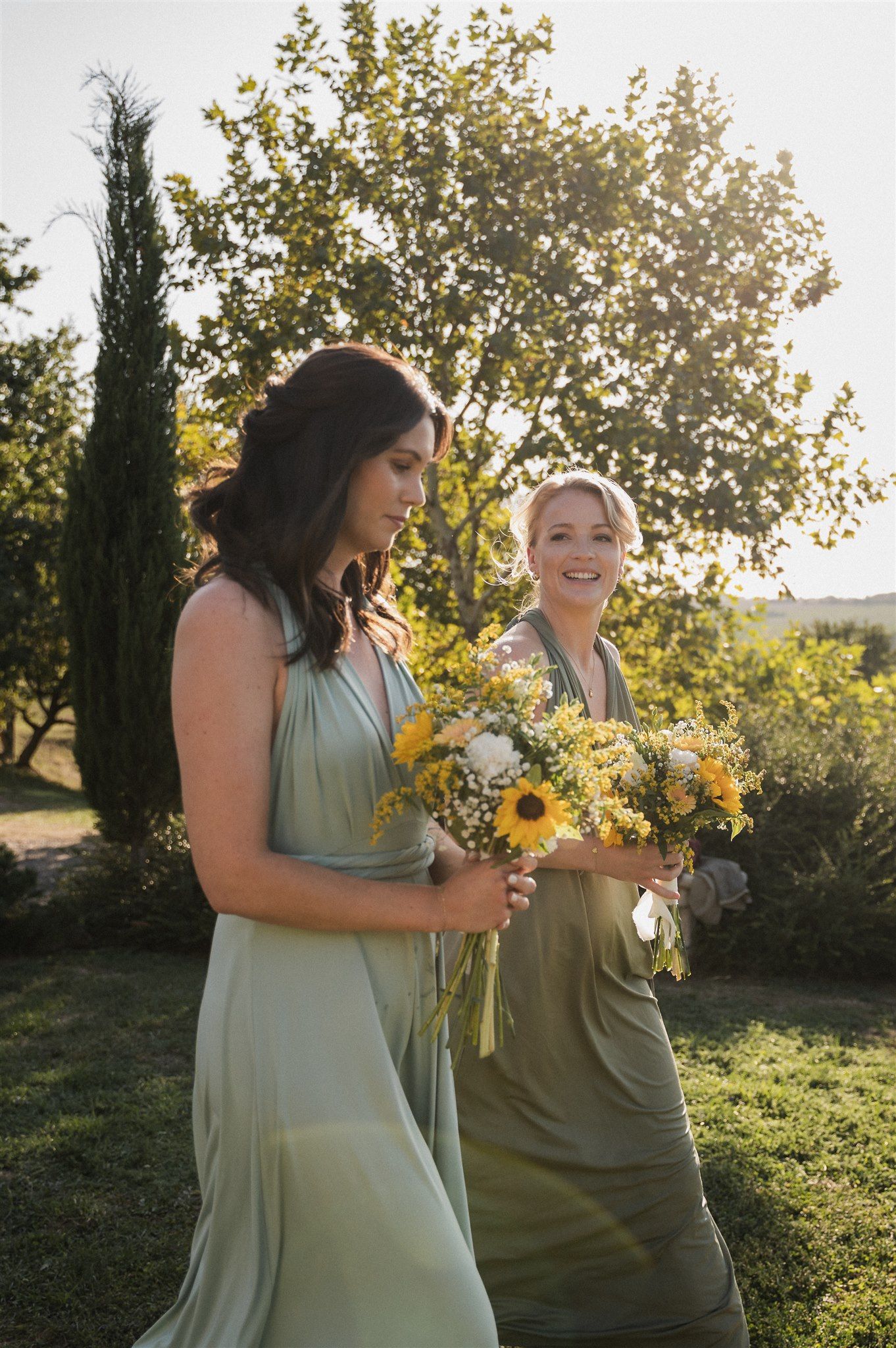 Wedding party members in mint green dresses holding sunflower bouquets in a garden setting.