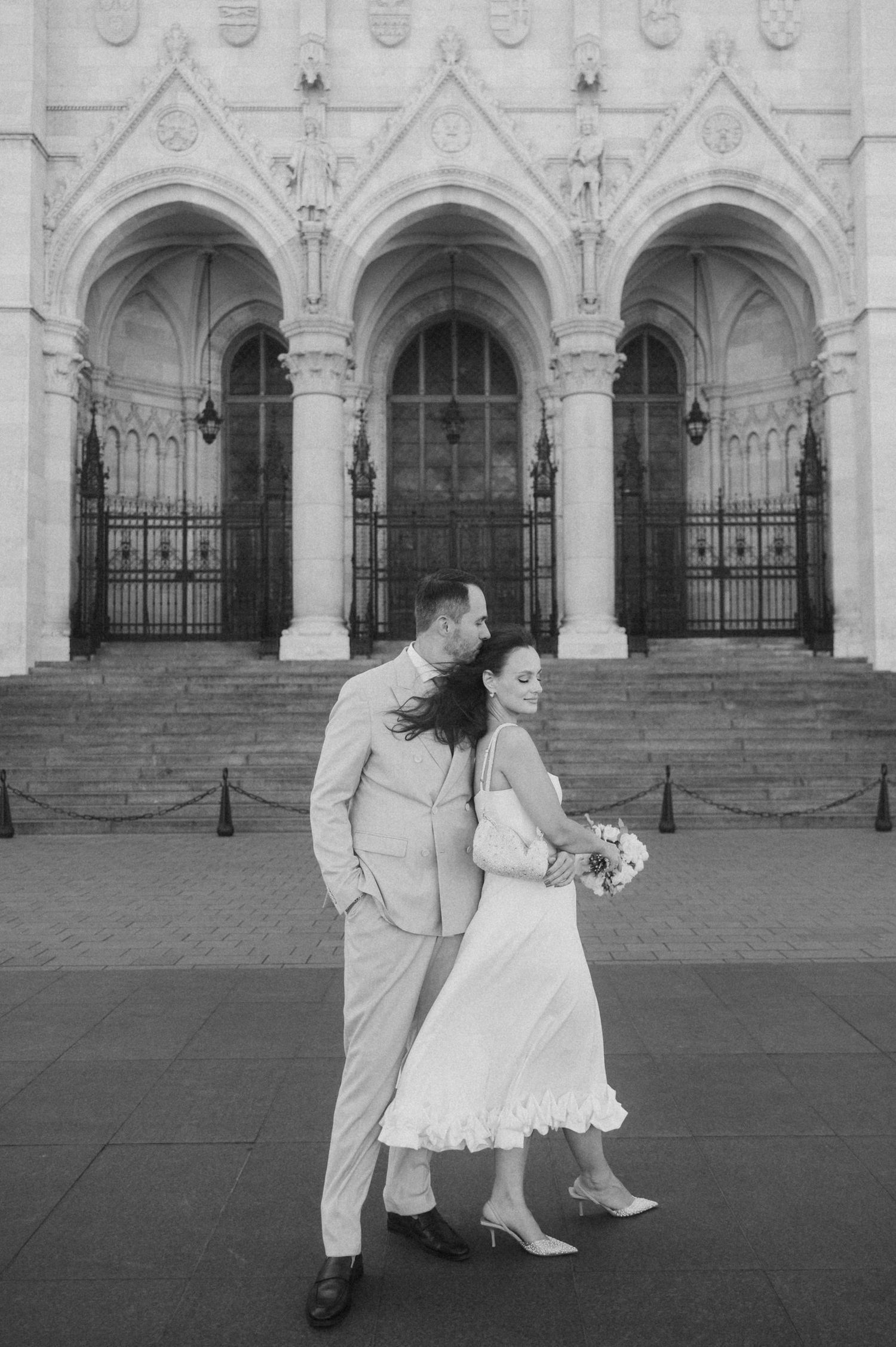 A black and white portrait of newlyweds posing before ornate church architecture.
