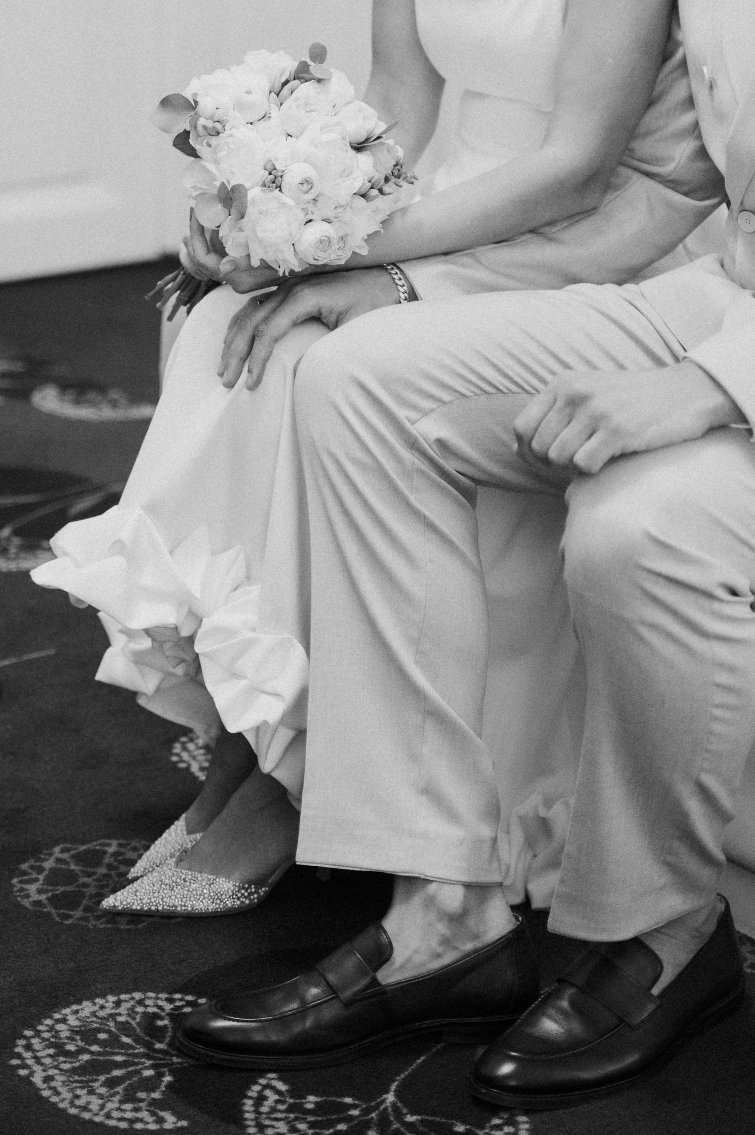 Close-up view of formal attire and shoes against a patterned carpet at a wedding.