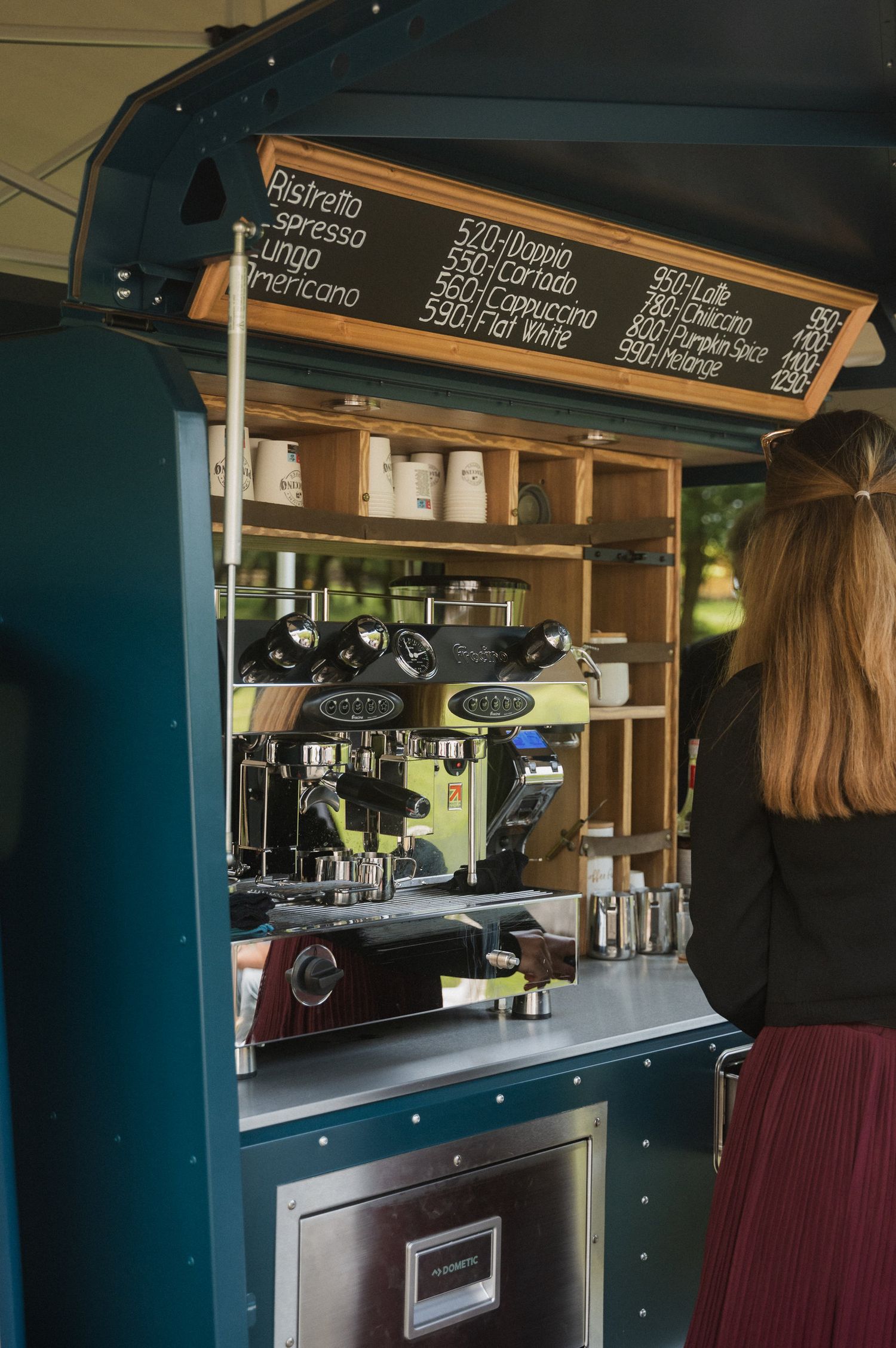 Mobile coffee bar interior with espresso machine and menu board mounted in dark blue cabinetry.