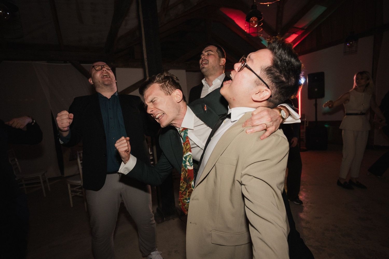 A group of people dancing and having fun at a dimly lit party venue with red lighting in the background.