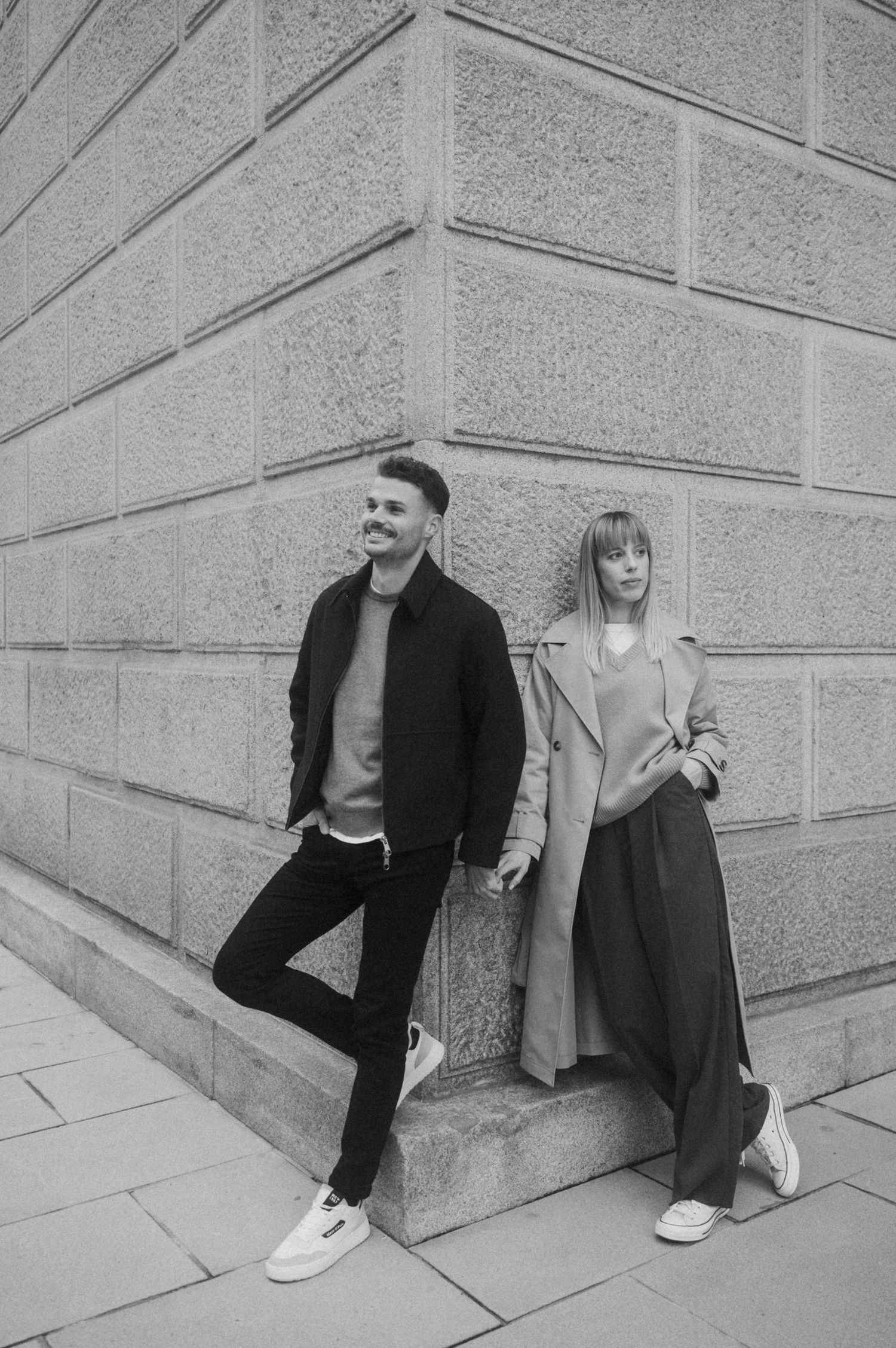 A couple sits together against a stone wall in a series of black and white candid photographs.