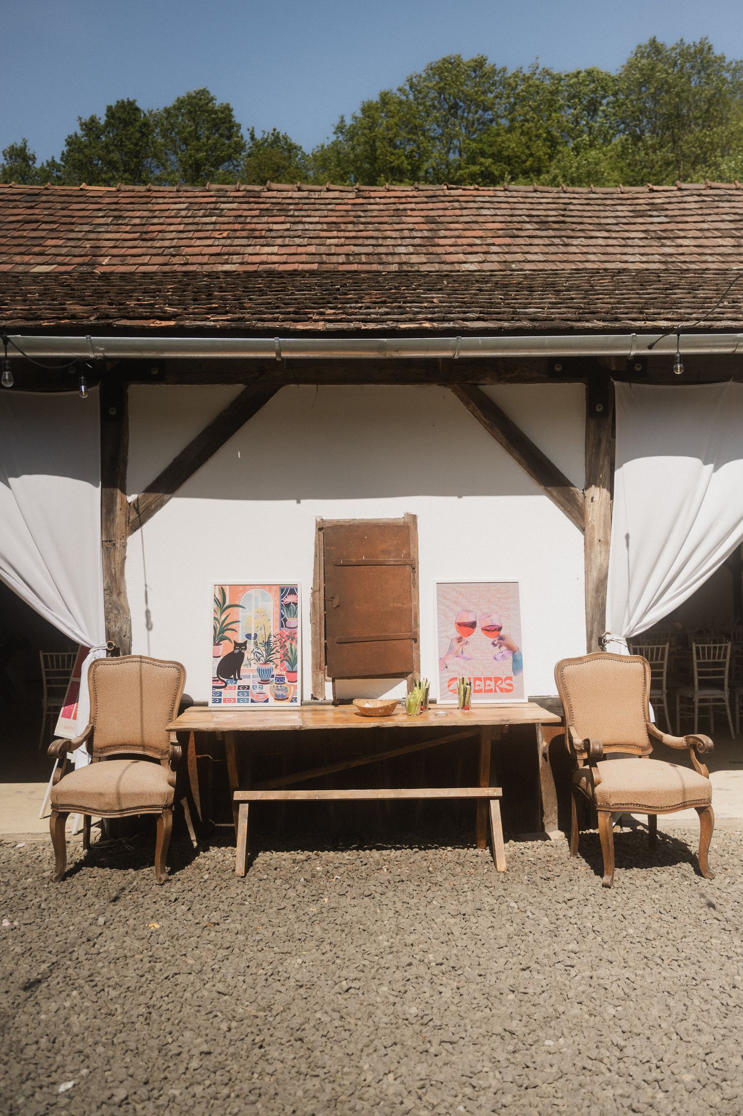 Wooden outdoor furniture set with beige cushions arranged in a row against a white wall with a rustic shingle roof.