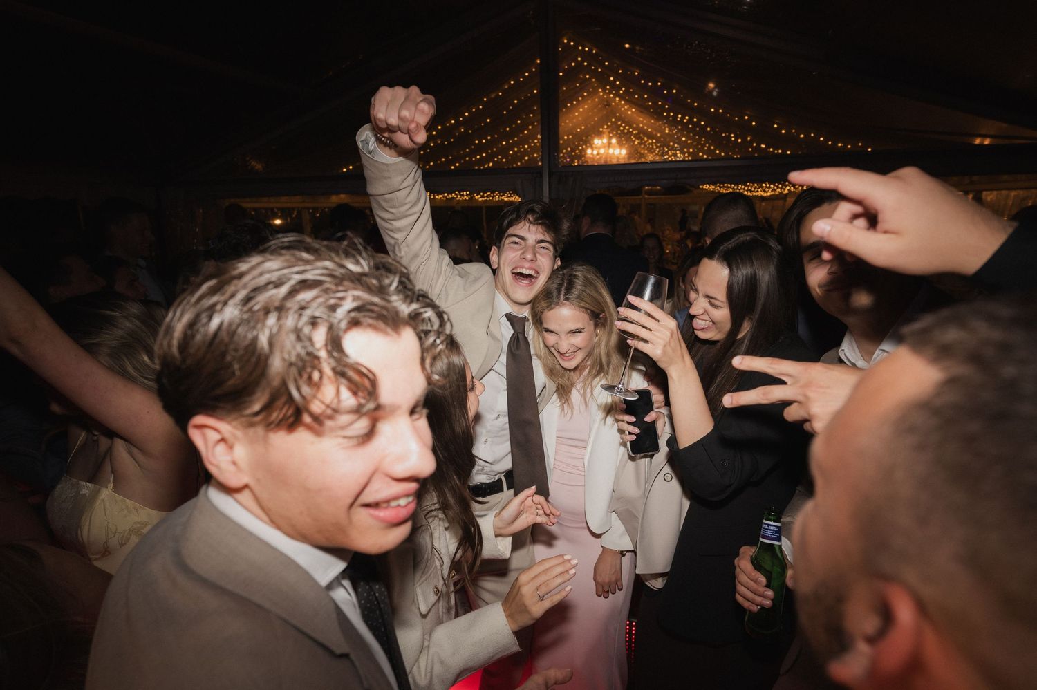 Guests celebrate joyfully on the dance floor at a lively evening wedding reception.