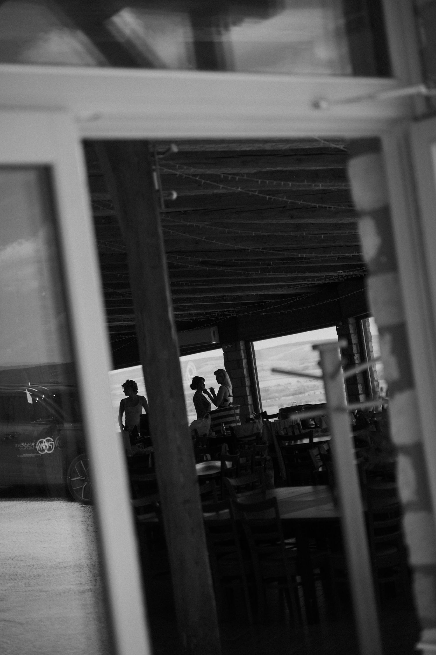 Silhouettes of two people conversing inside a restaurant, captured through a window in black and white.