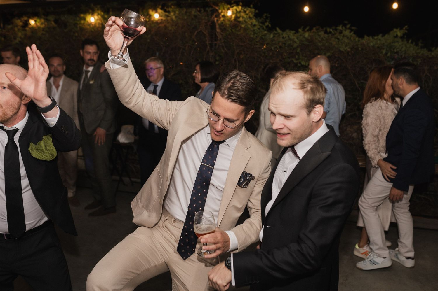 Wedding guests dance and celebrate during an evening reception with string lights overhead.
