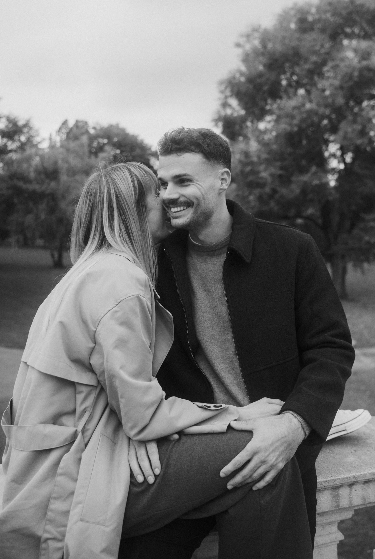 A romantic couple sitting together outdoors sharing tender moments in a black and white photo series.