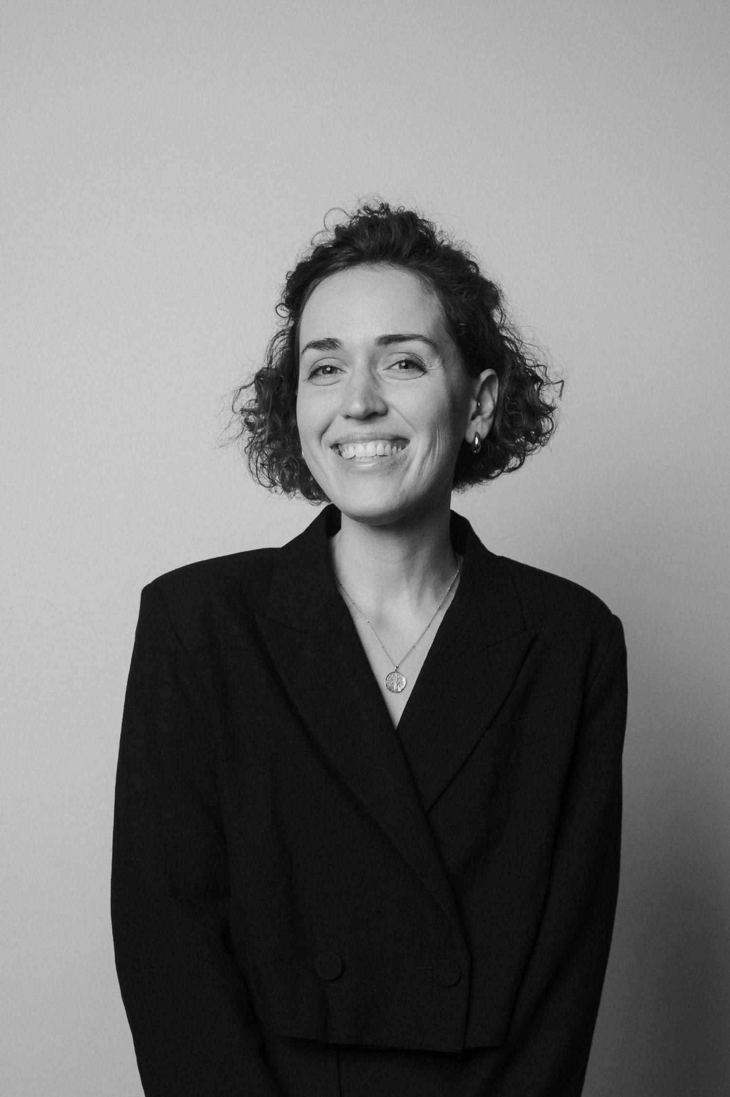A series of black and white portraits showing a person in a black blazer with curly hair expressing different emotions.