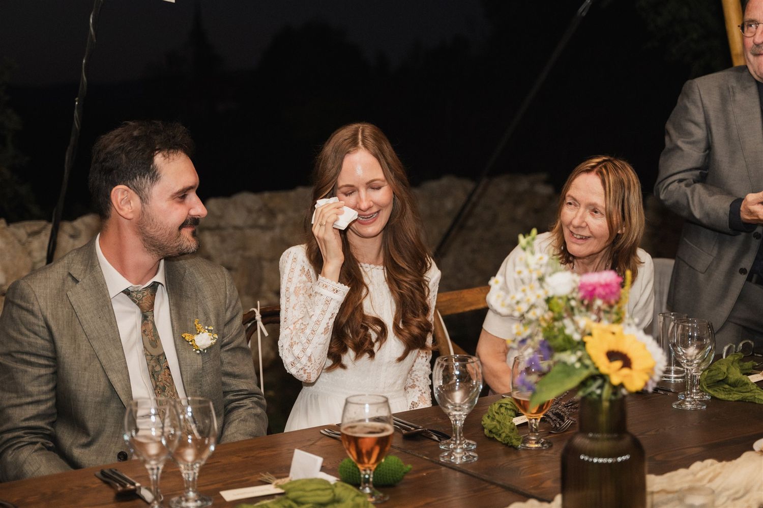 Wedding reception dinner table with guests enjoying conversation under dim lighting.