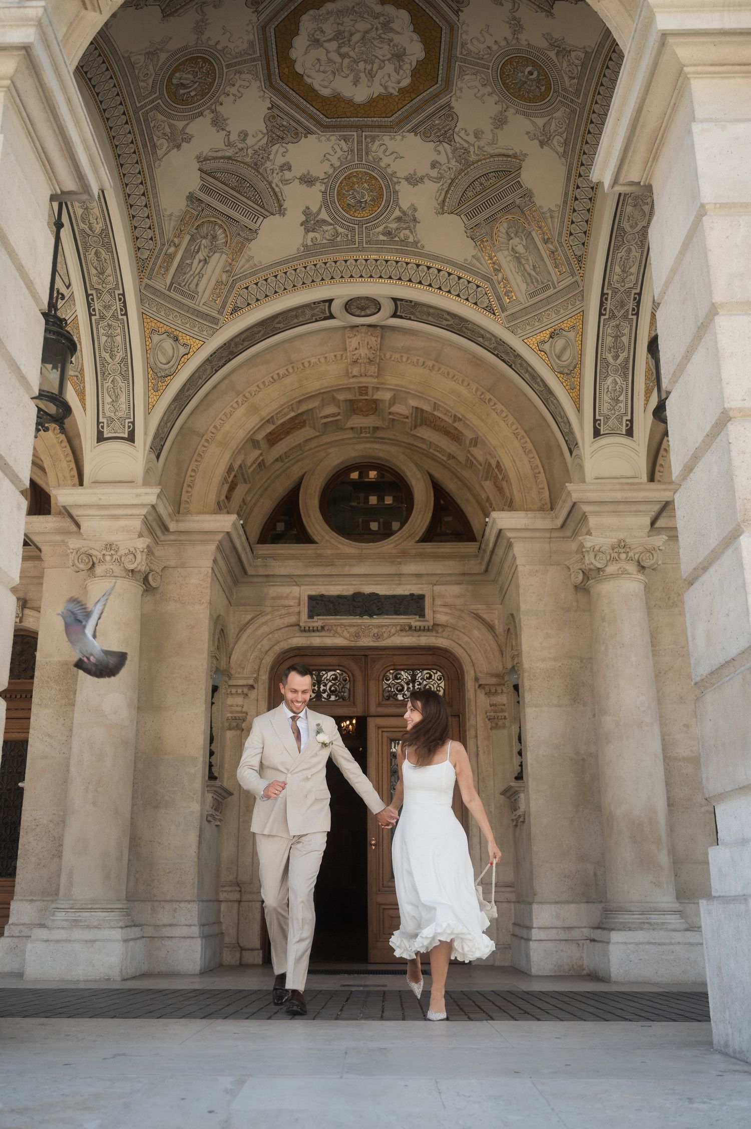 Wedding couple dances beneath ornate vaulted ceilings of historic colonnade.