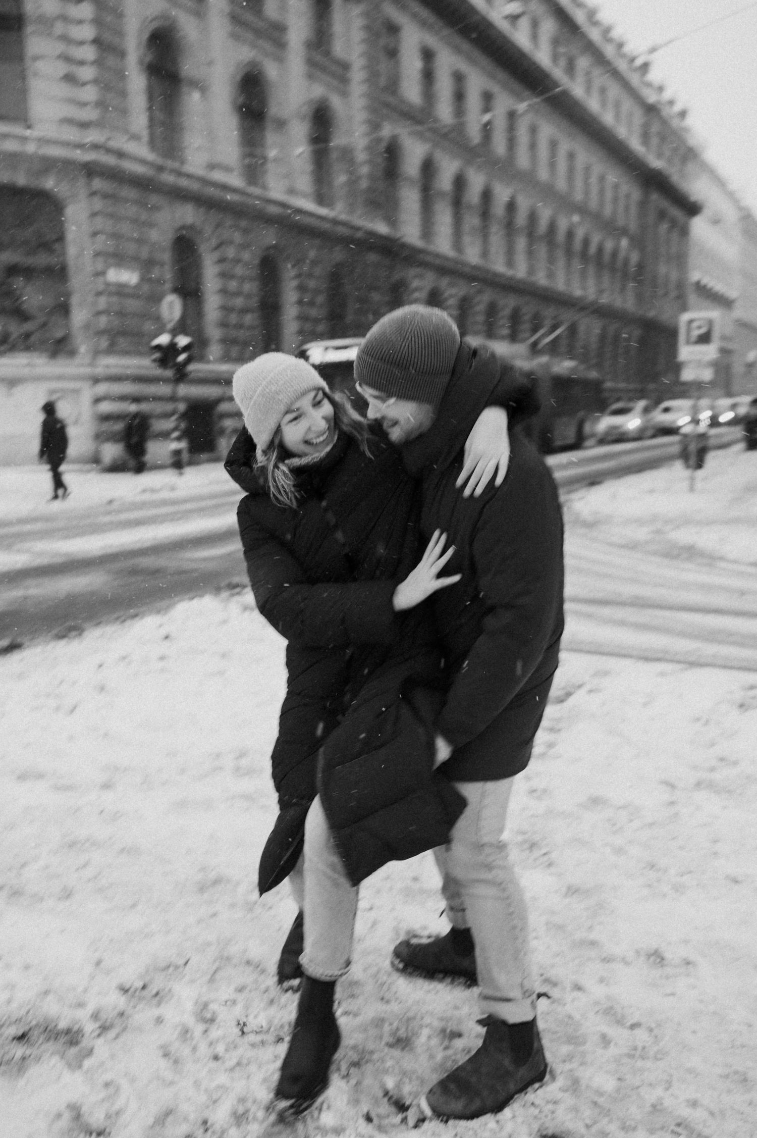 Two people playing in the snow near historic buildings.