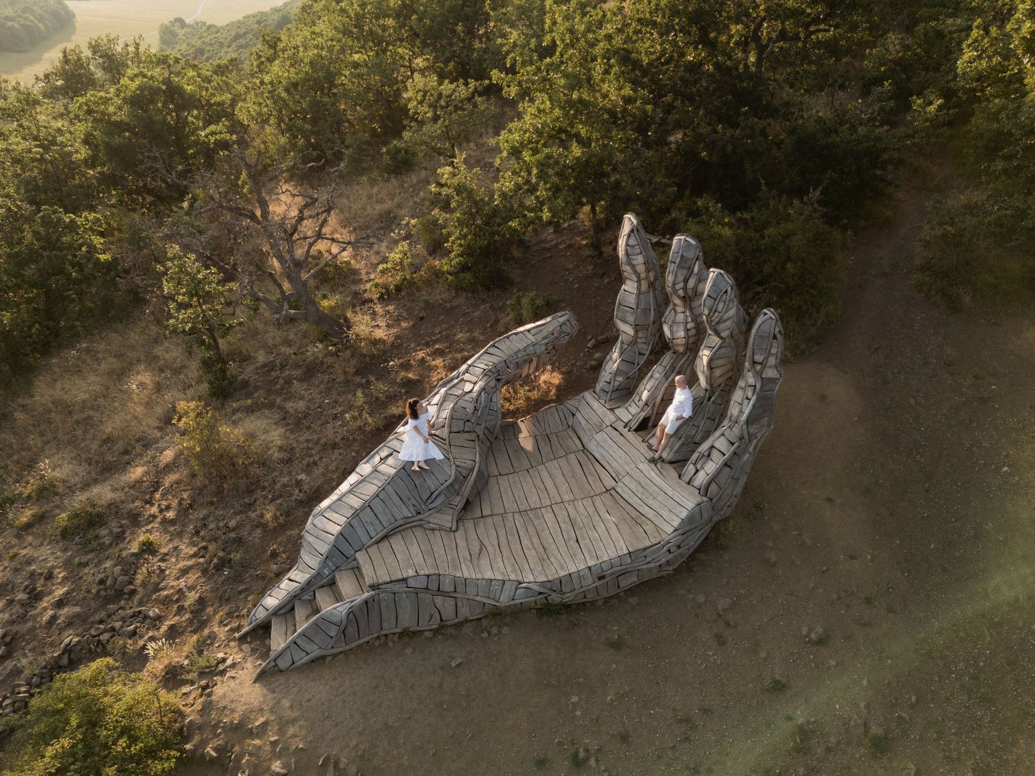 A large concrete sculpture of a reclining figure lies among trees and grass in an outdoor park setting.