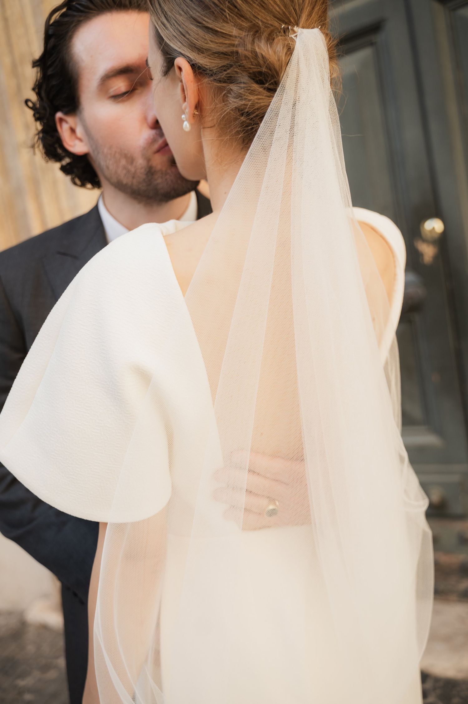 Elegant wedding couple embracing in front of classic European architecture.