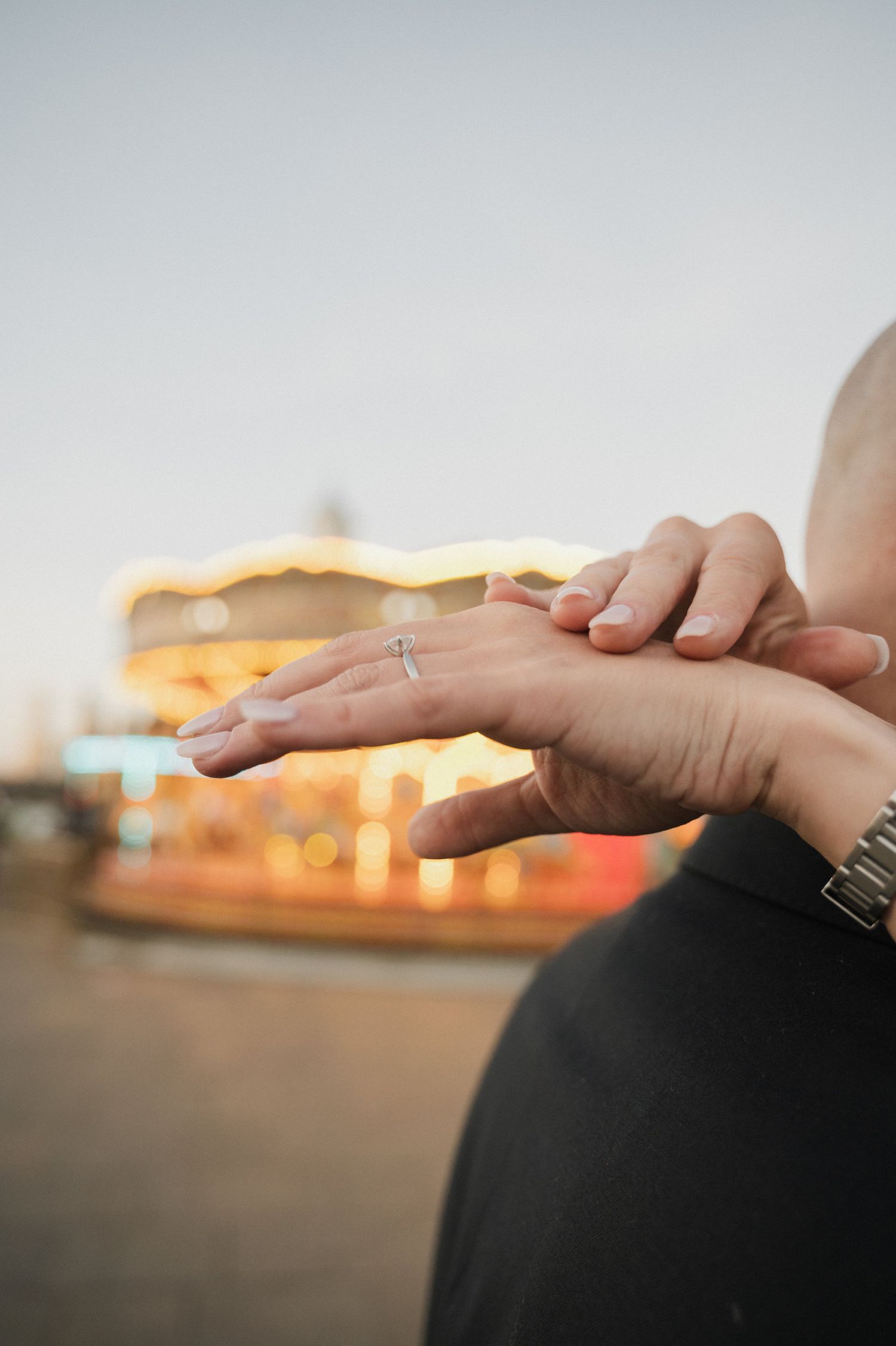 Gentle hands touch against a sunset backdrop with soft bokeh lights.