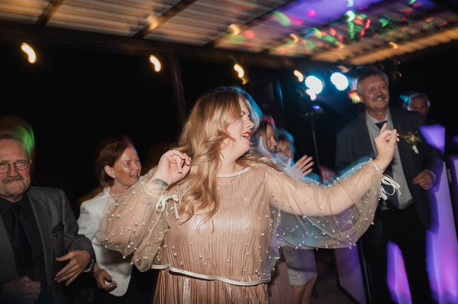 Wedding guests celebrate on a dance floor illuminated with colorful lights and decorations.