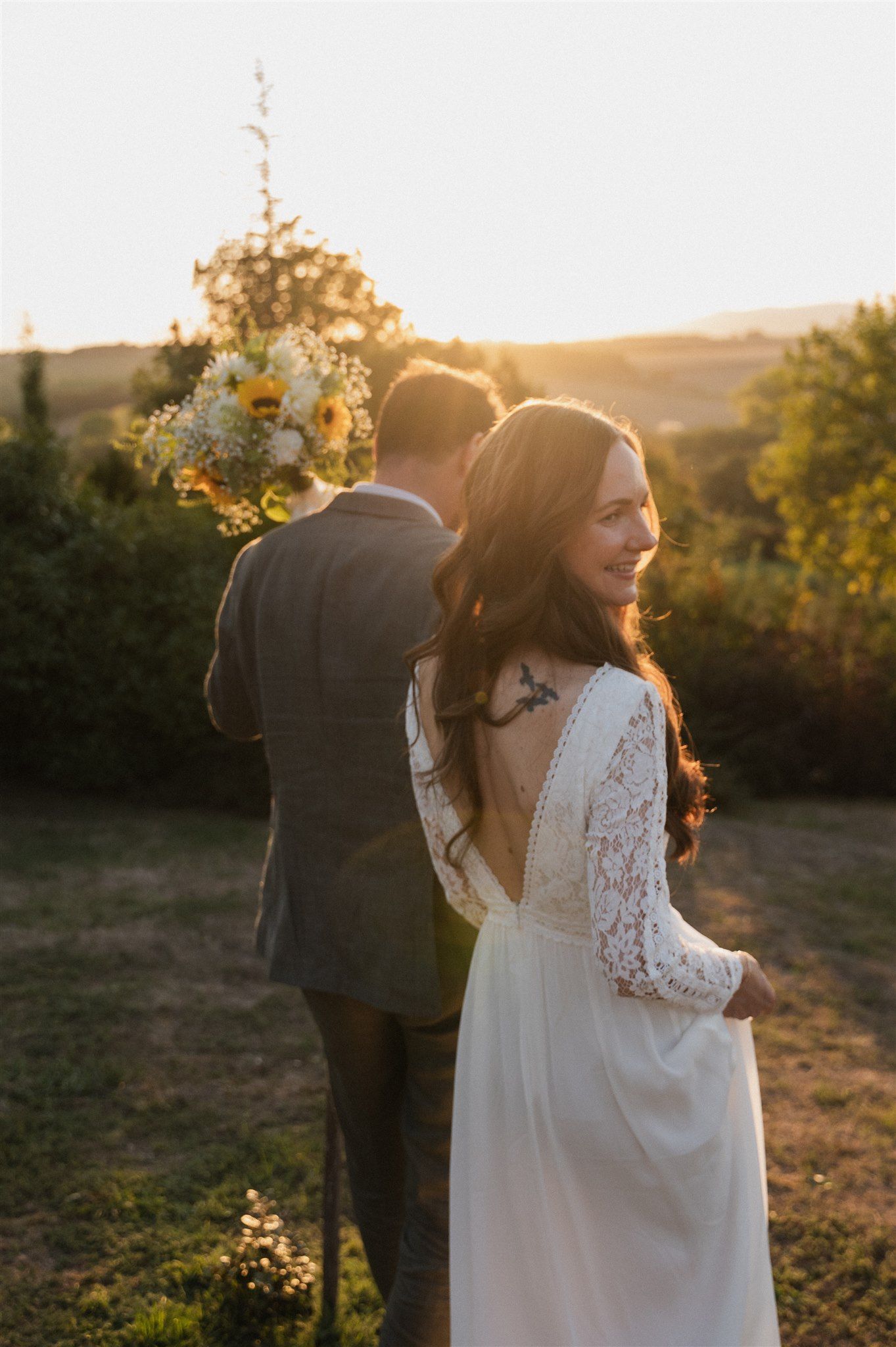 A couple shares a tender moment at sunset with a bouquet of wildflowers.