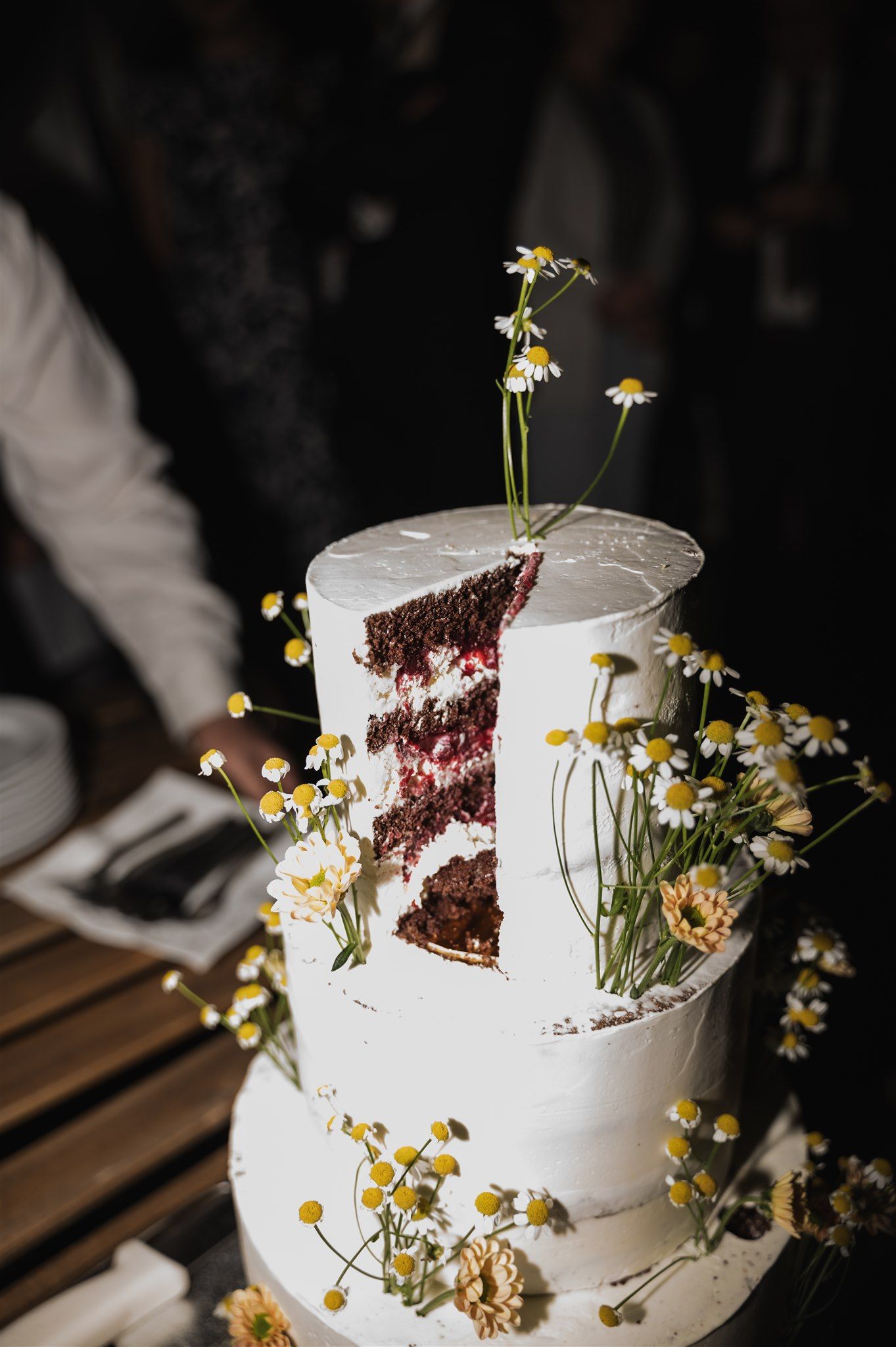 White wedding cake decorated with delicate yellow wildflowers and exposed chocolate layers.