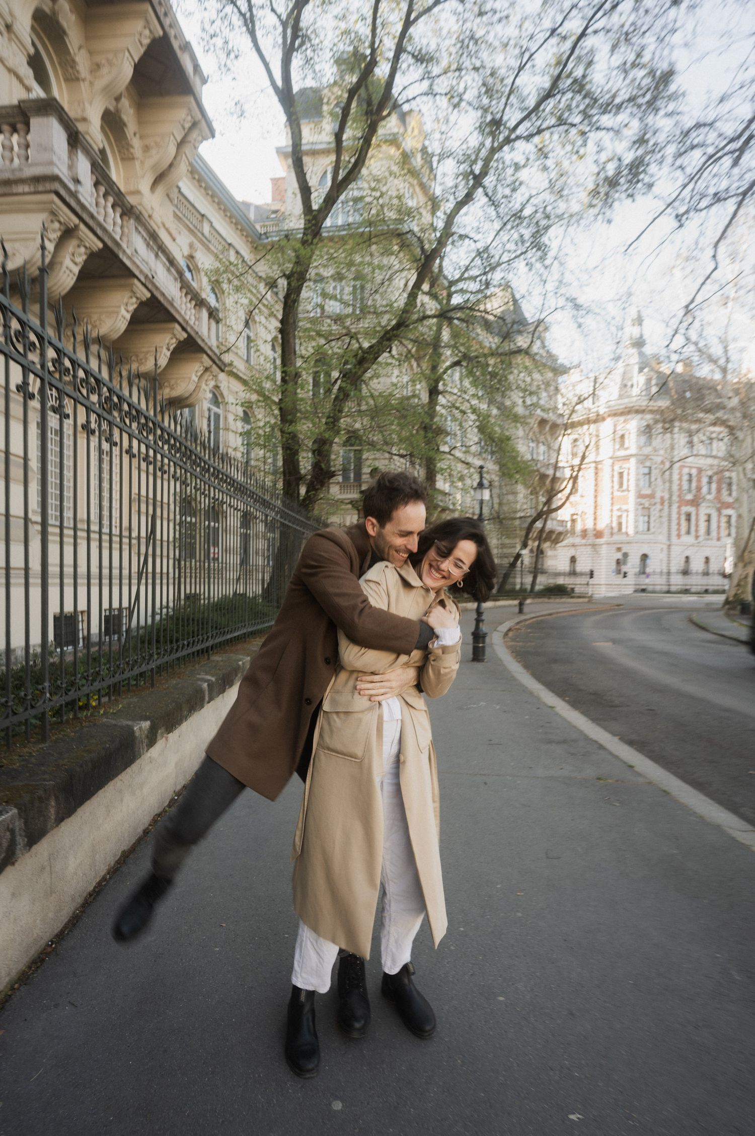 A couple dances playfully on a historic street lined with elegant architecture and iron railings.