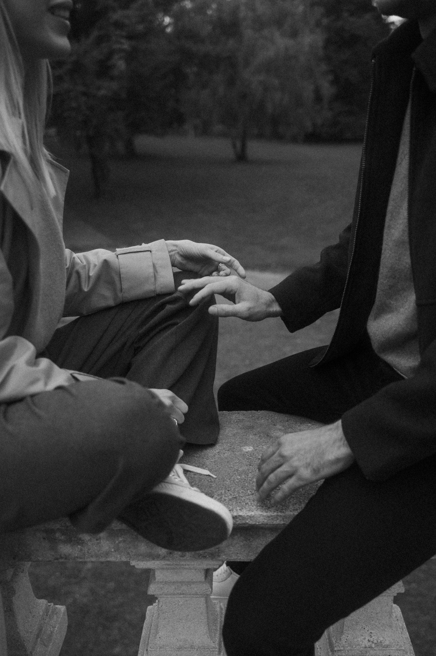 Close-up black and white shots of hands resting on a stone railing outdoors.