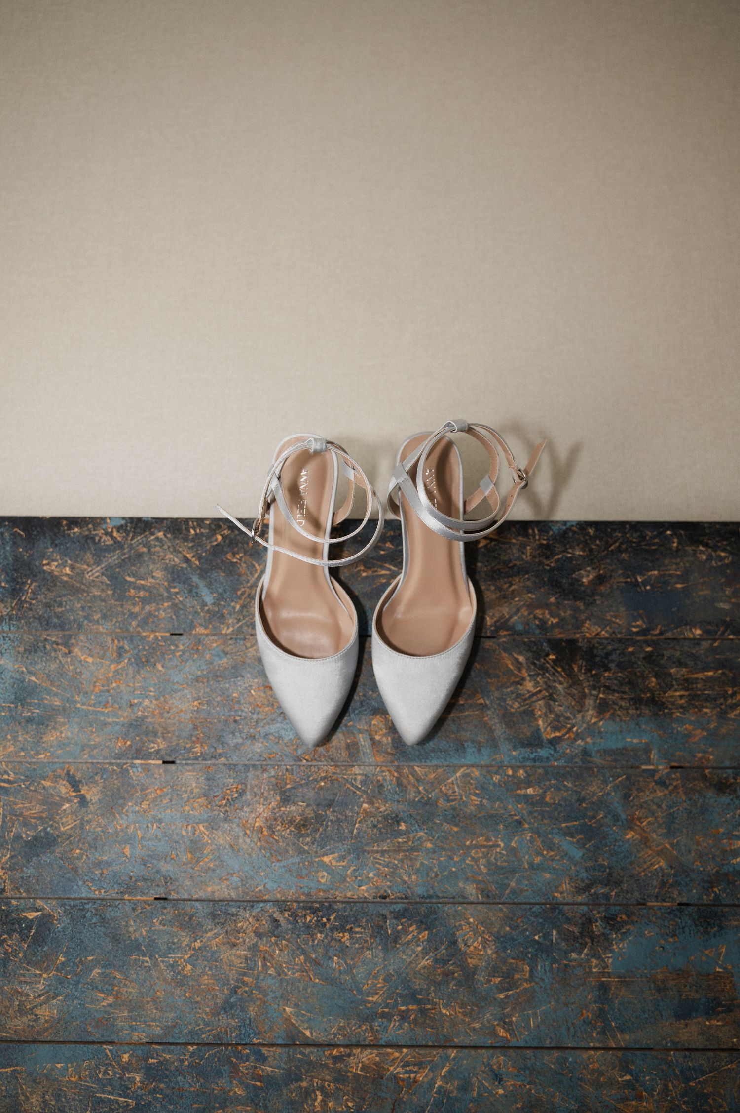 Three identical pairs of elegant nude and white pointed-toe slingback heels arranged on a rustic blue wooden floor.