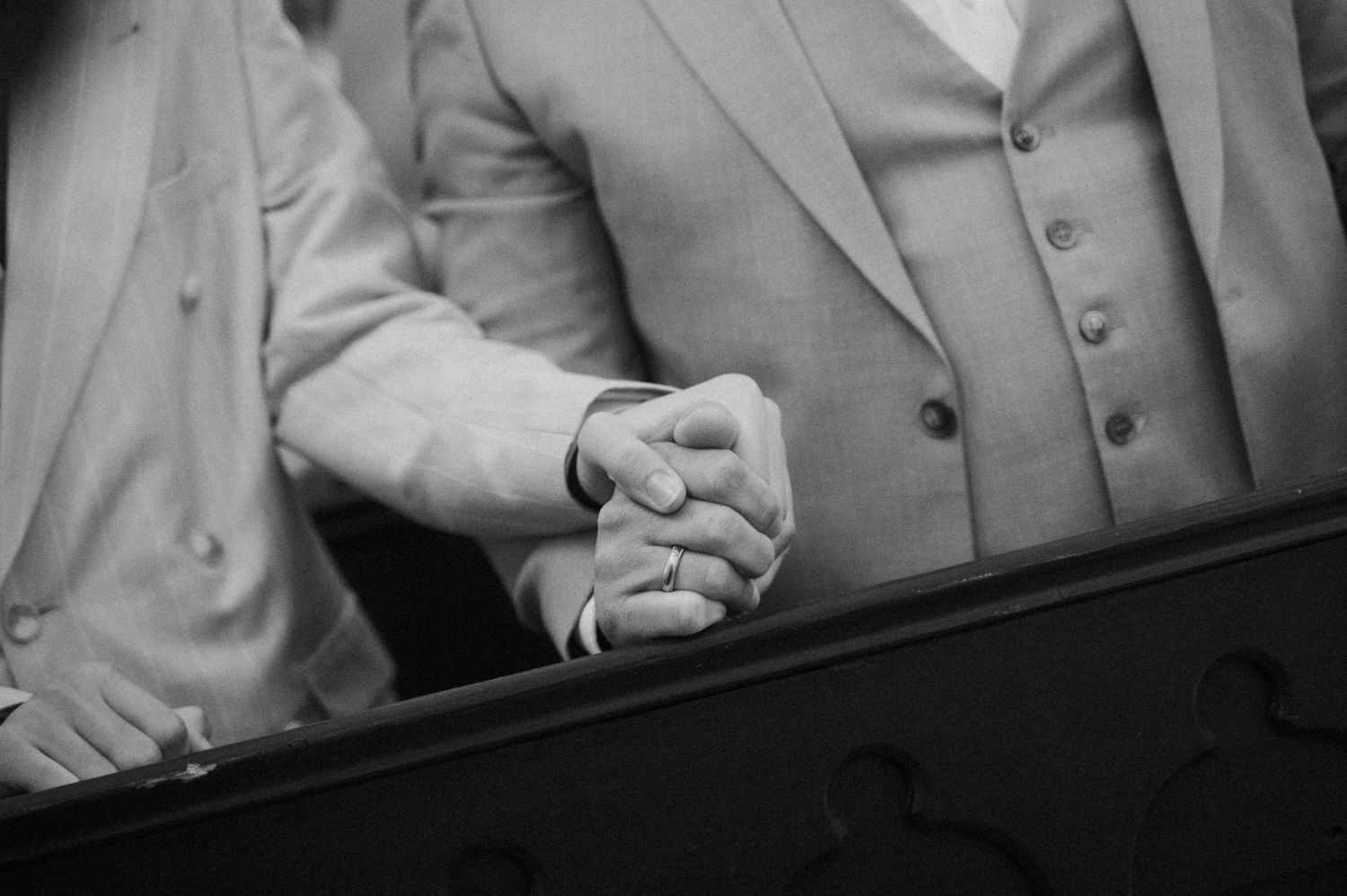 Close-up black and white photo of wedding guests holding hands in prayer during church ceremony.