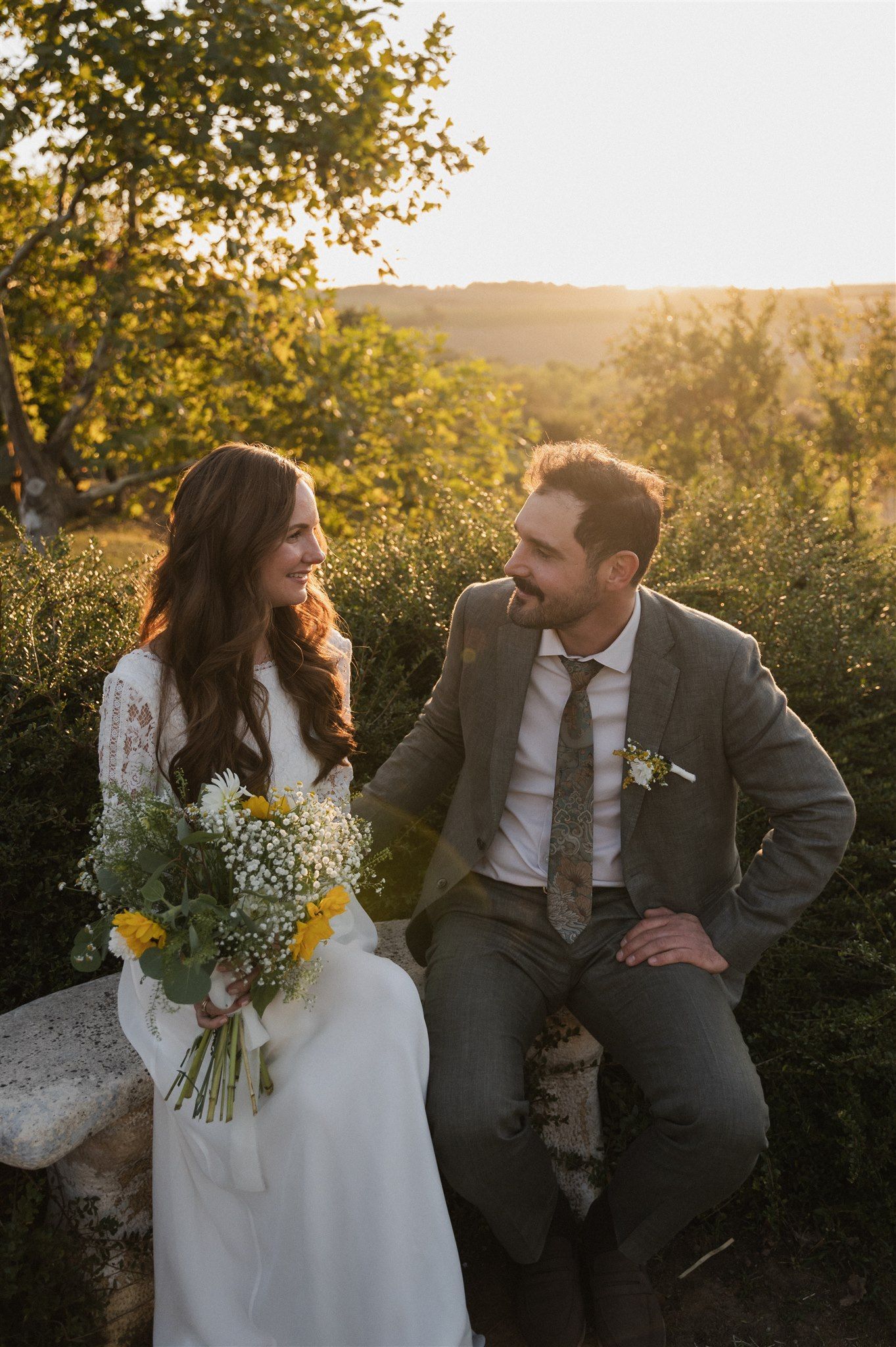Newlyweds sharing a tender moment in golden sunset light with rustic bouquet.