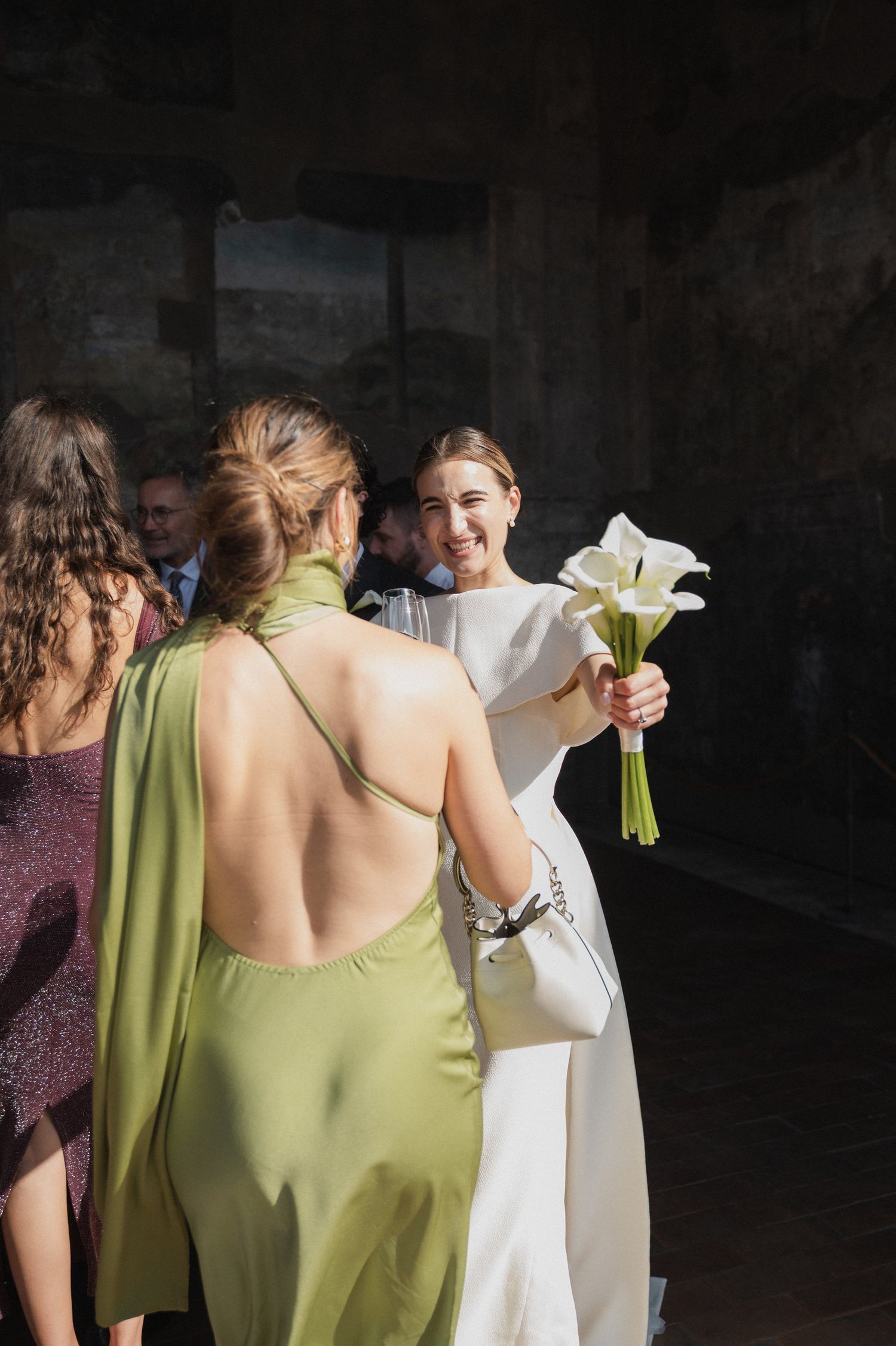 Wedding party members in green dresses gather with white calla lily bouquets.