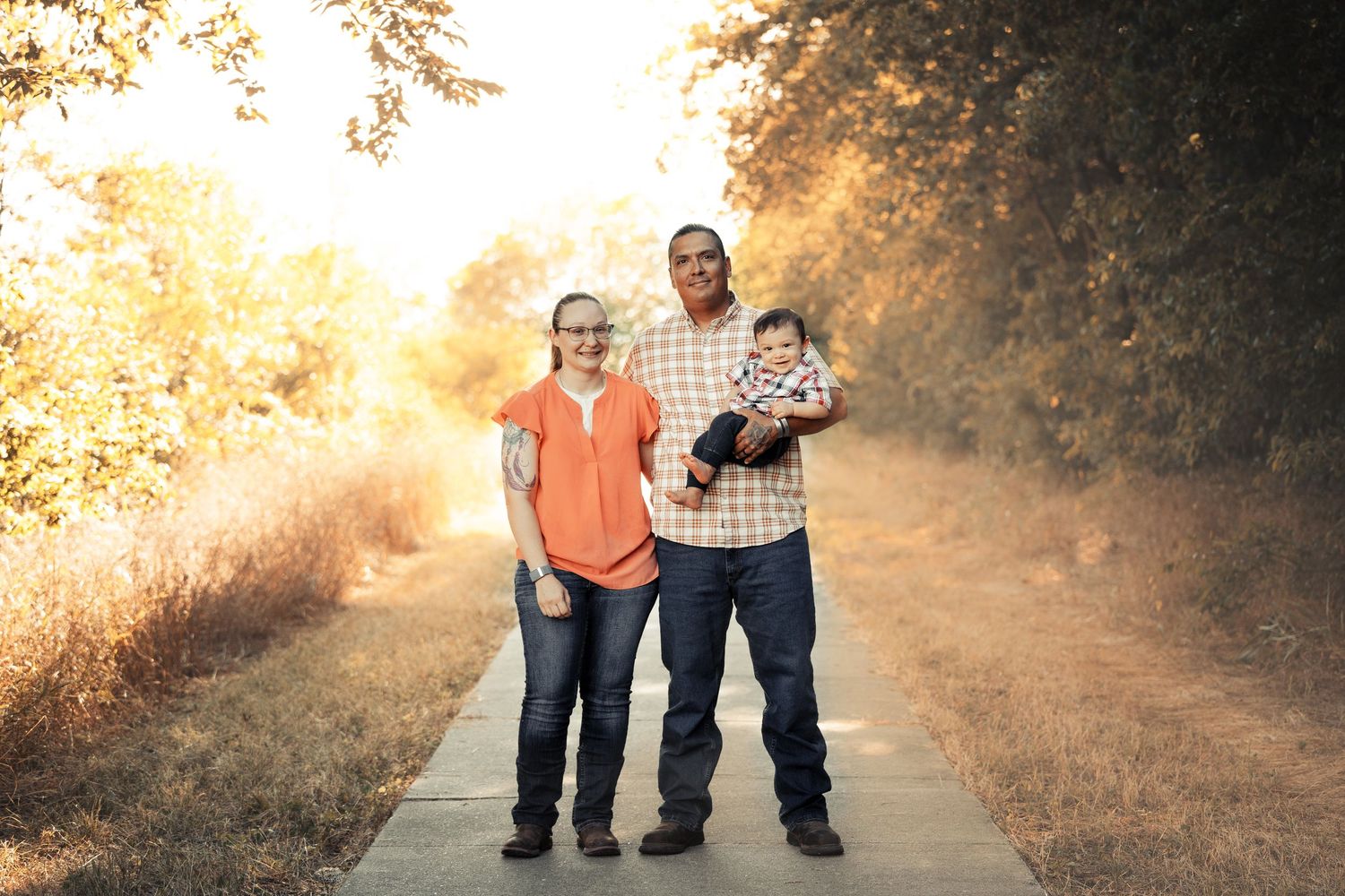 Family walking together on sunlit autumn path through trees.