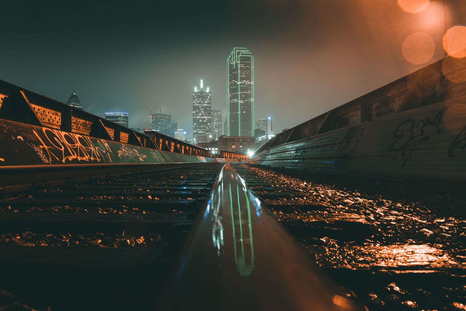 Moody cityscape with reflective puddle and illuminated skyscrapers at night.