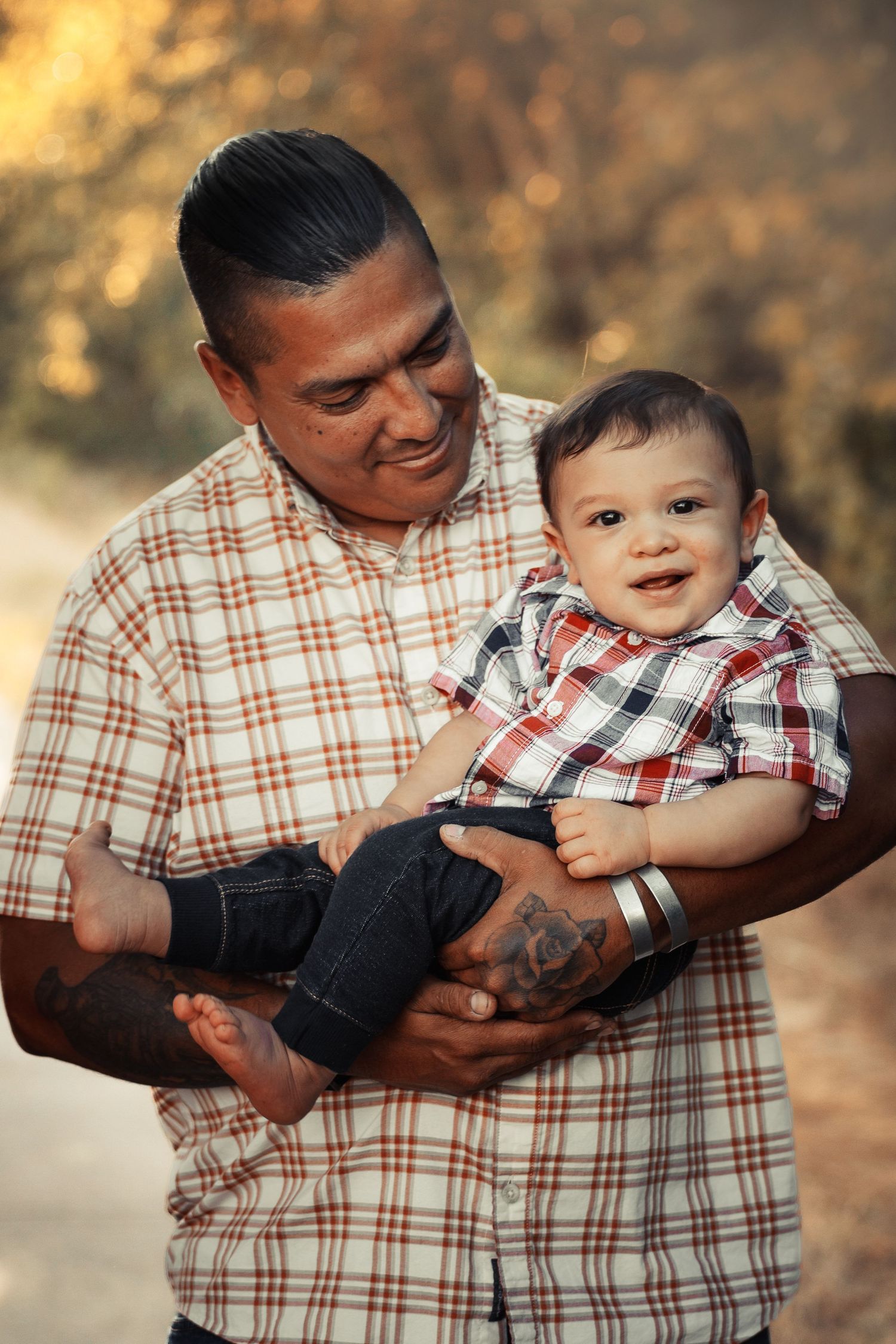 Parent holding baby in plaid shirt against warm autumn backdrop.