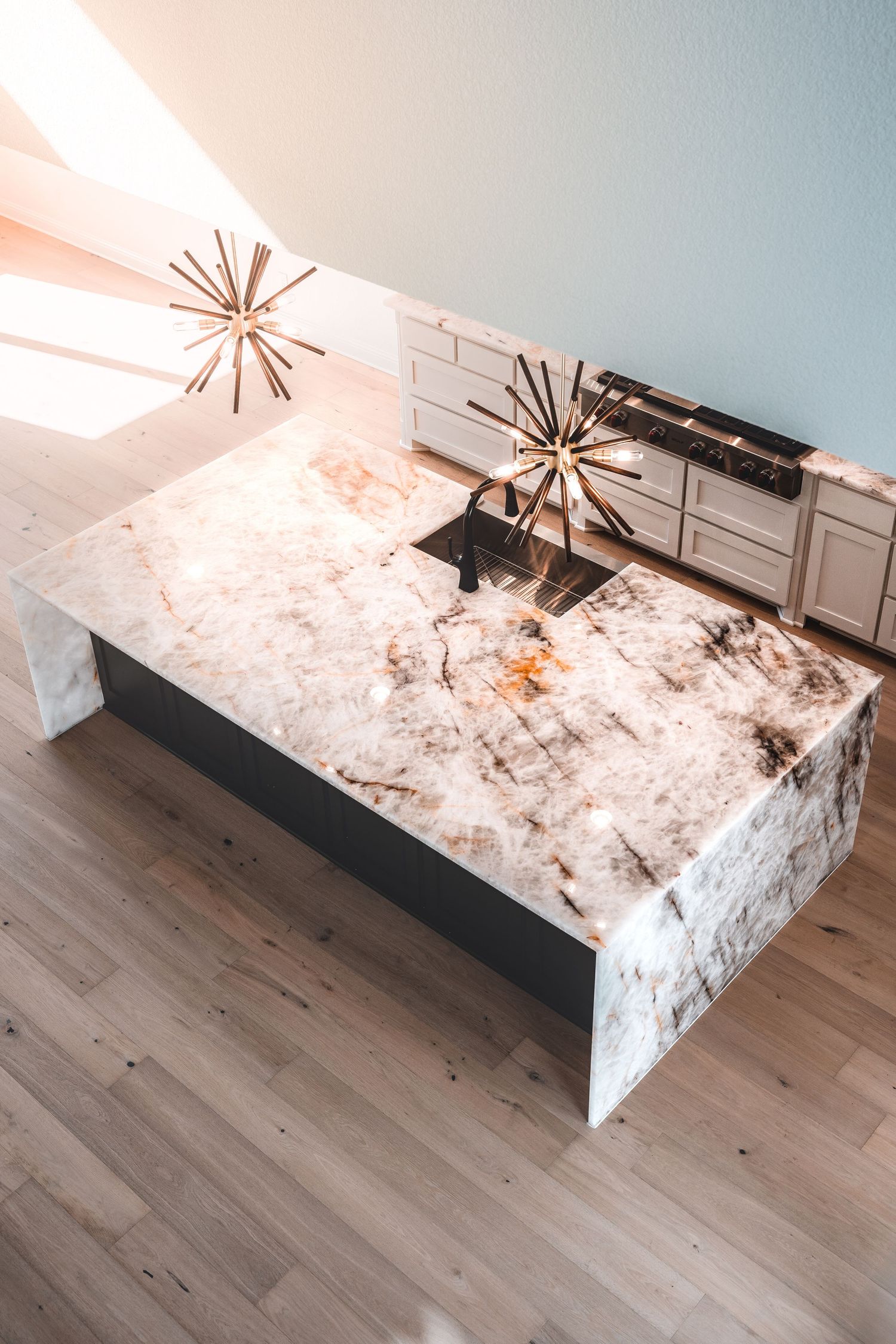 Luxury kitchen space with geometric light fixture and dramatic marble waterfall countertop.