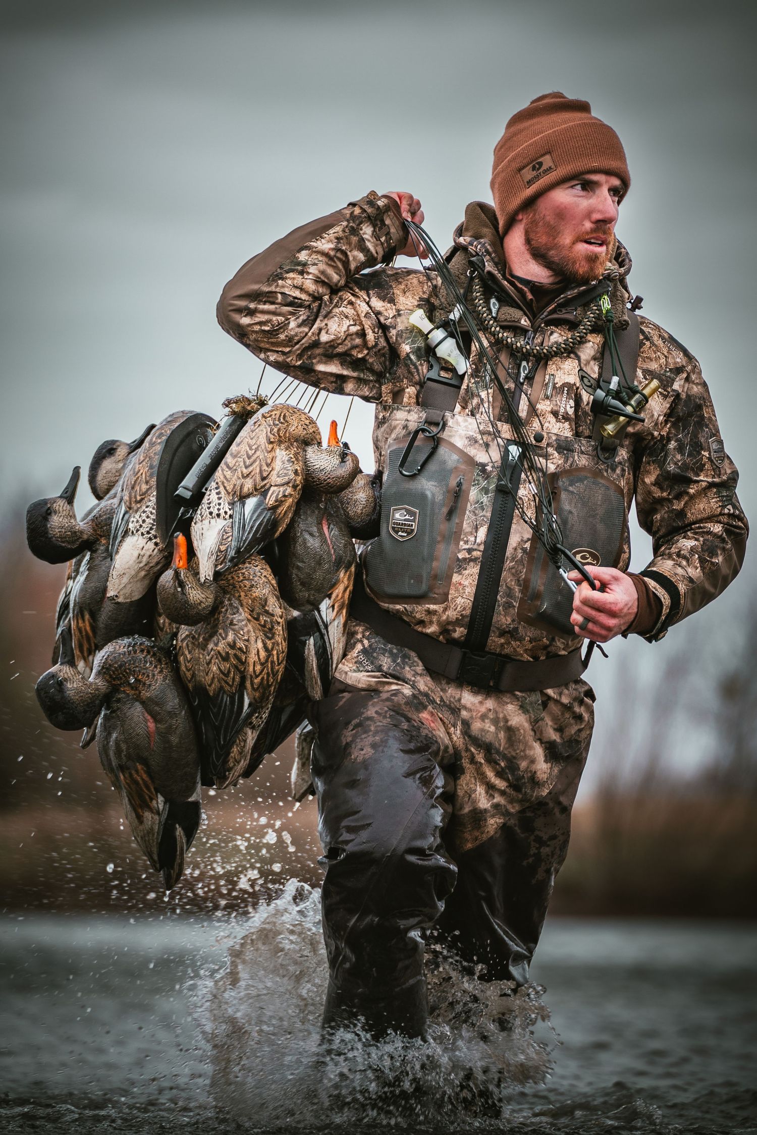 Duck hunter wading through shallow water in camouflage gear creates dramatic splashing motion.