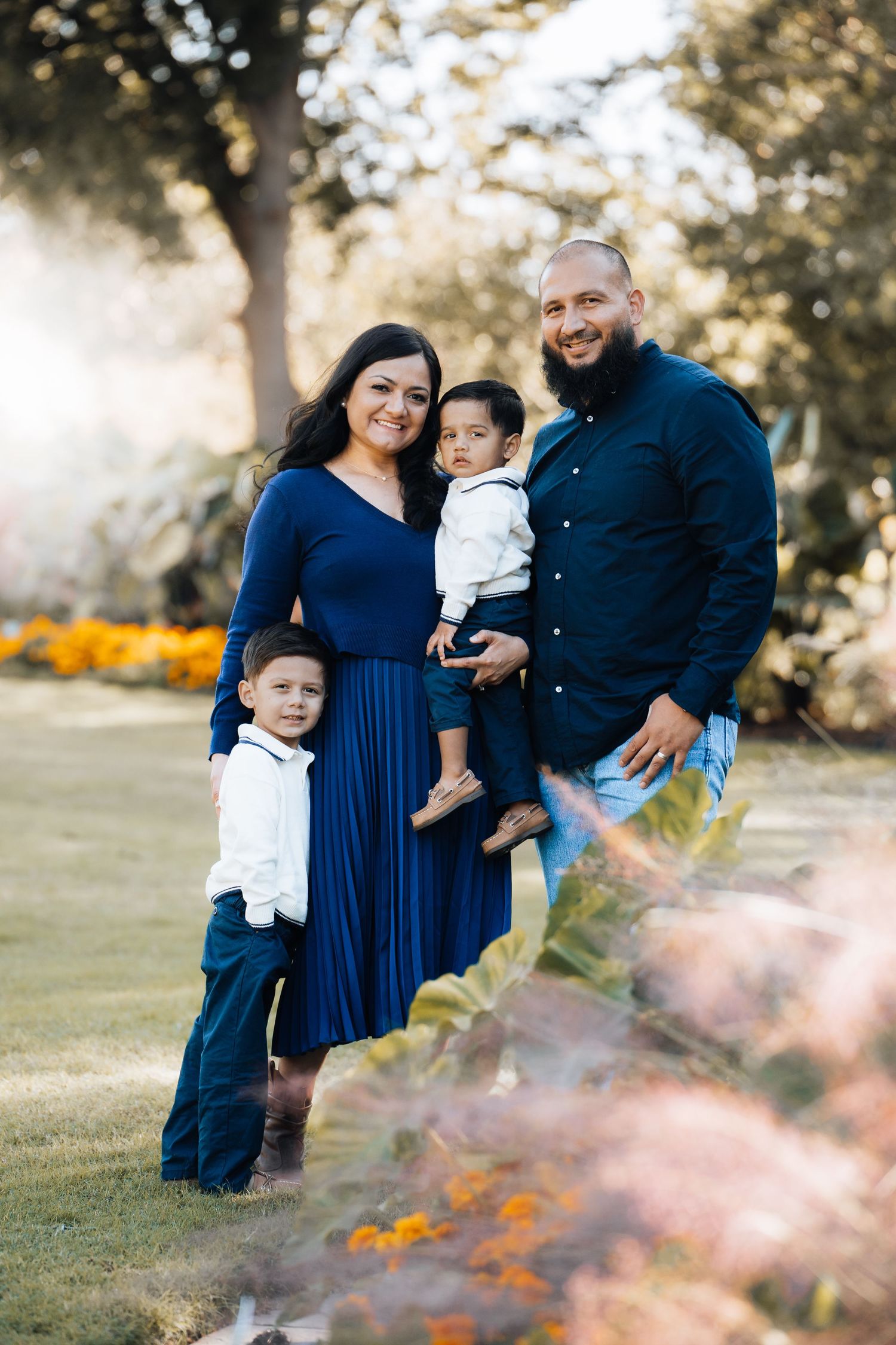 A family in coordinating navy and white outfits poses together on a grassy field during golden hour. Dallas arboretum family photography.