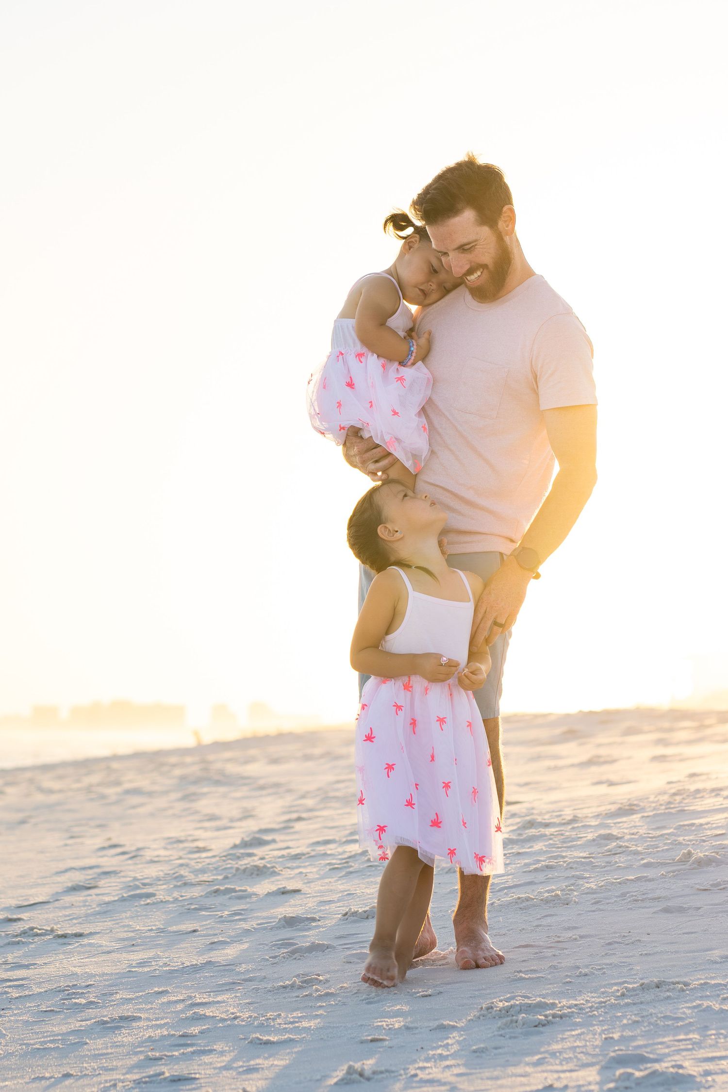 A tender moment captured on a sunny beach with light glowing behind the subjects.