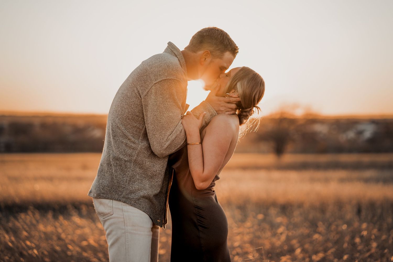 Romantic couple embracing in a sun-drenched field during golden hour.