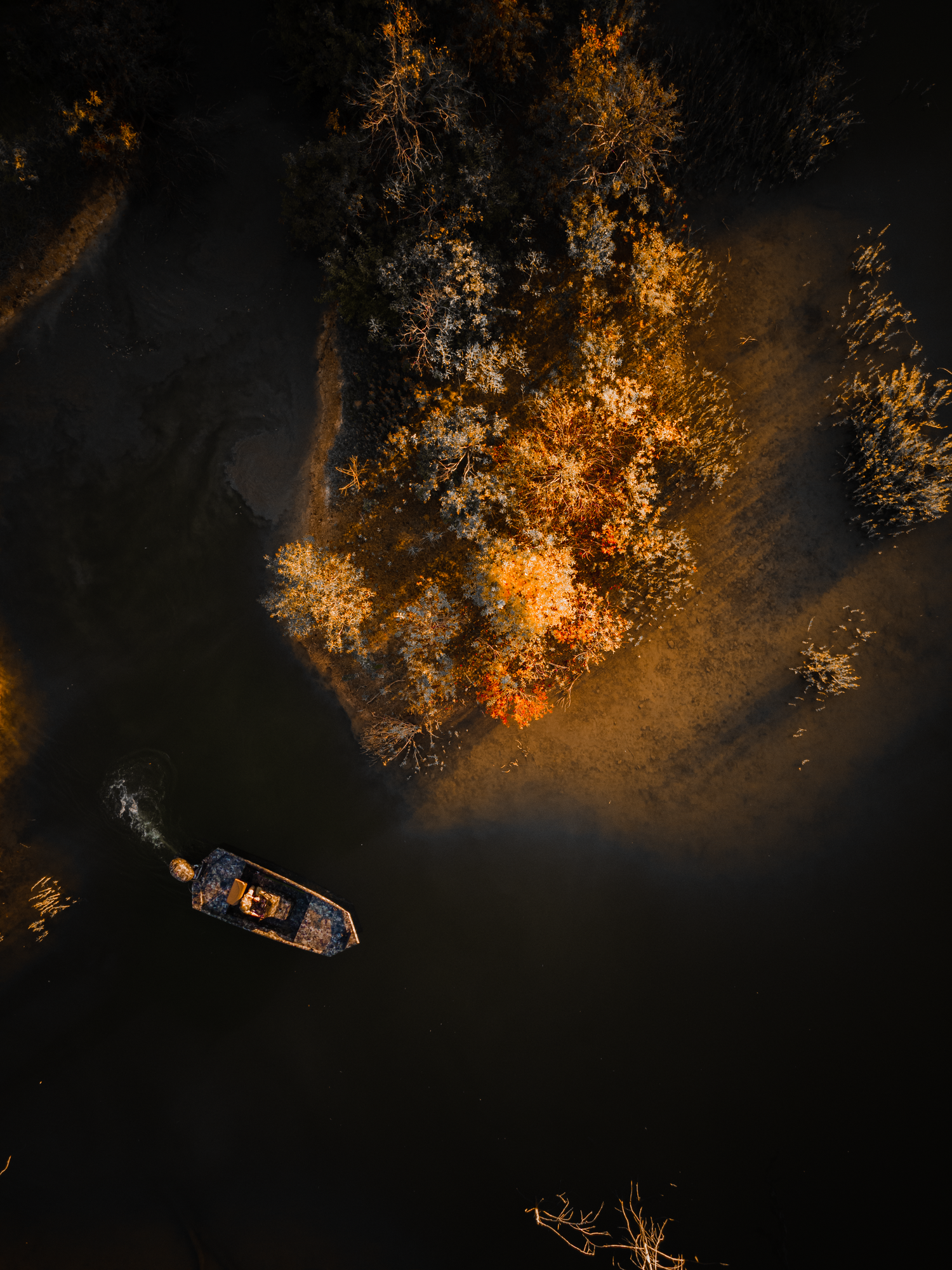 Overhead drone shot of small boats floating on dark water with glowing orange foliage along the shore.