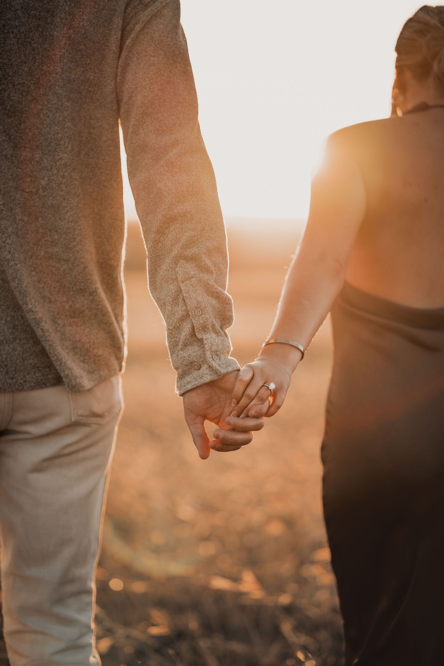 Close up of two hands holding each other against a warm sunset backdrop.