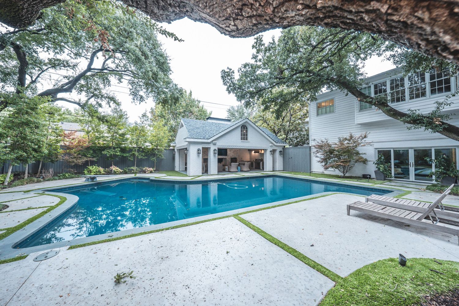 Backyard swimming pool and patio area surrounded by landscaping and mature trees.