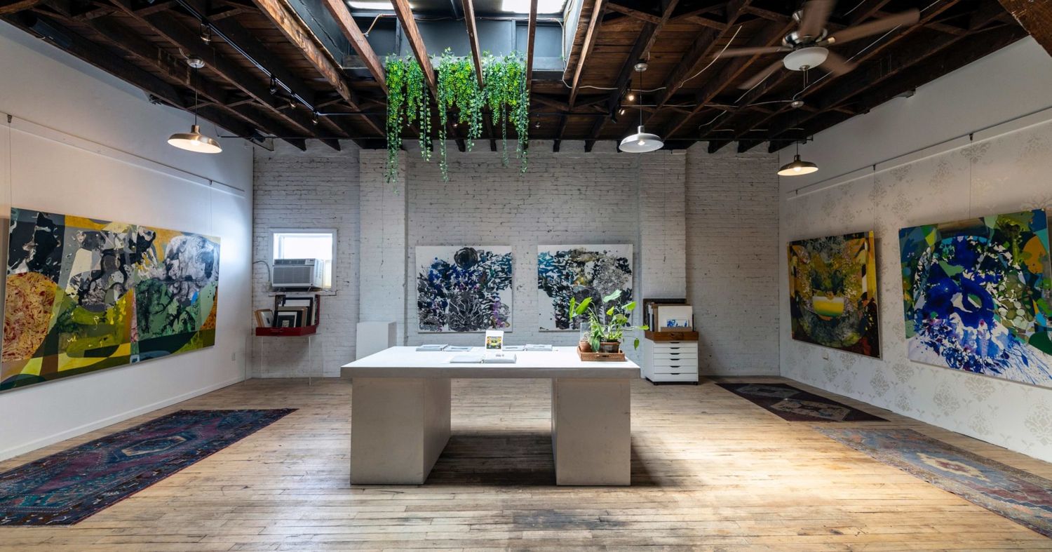 Art gallery space with exposed ceiling beams, wood flooring, and colorful artwork displays.