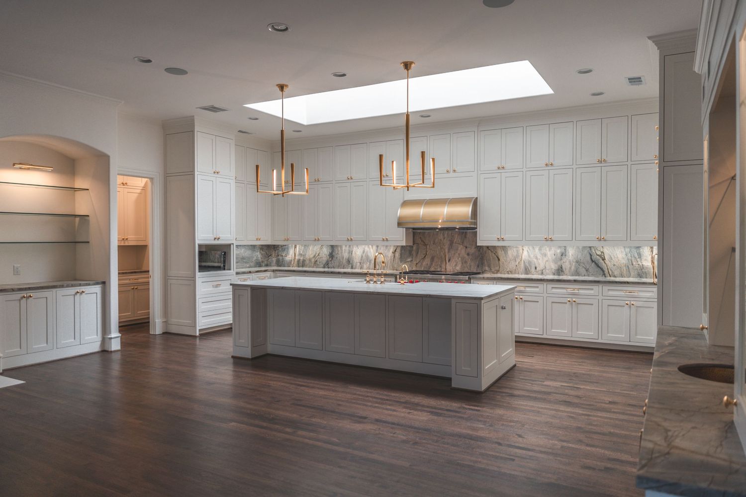Modern white kitchen interior with large island, pendant lights, and skylight creating bright open space.