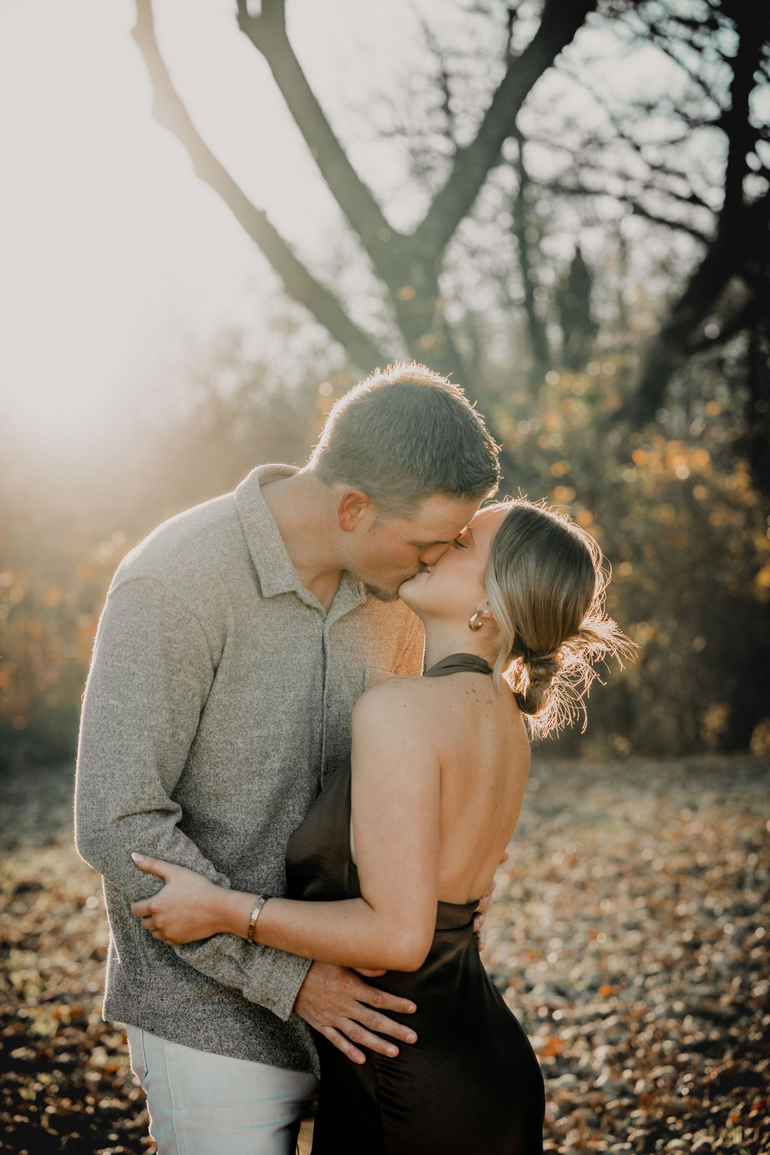 Romantic couple sharing an intimate moment in autumn sunlight with backlit glow through trees.