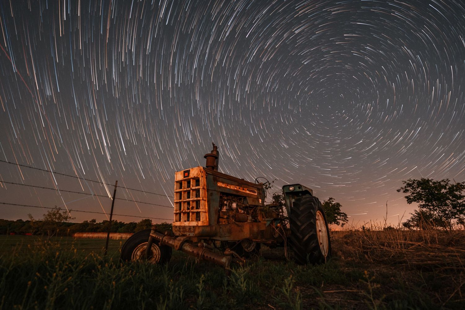 Star trails swirl in circular pattern around night sky with illuminated building in foreground.
