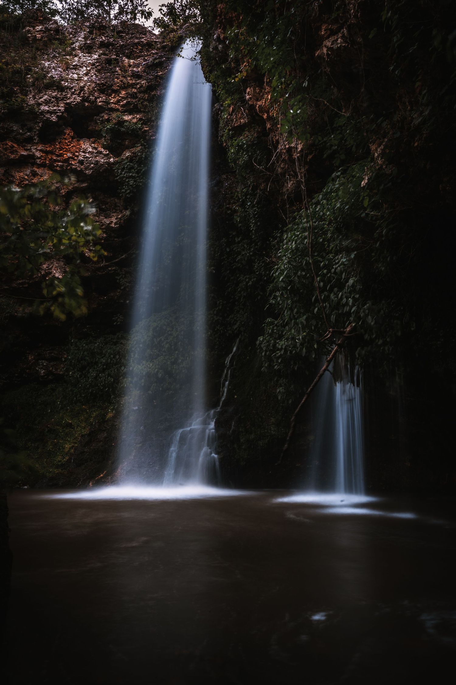 Majestic waterfall cascading down rocky cliff face in dark forest setting.