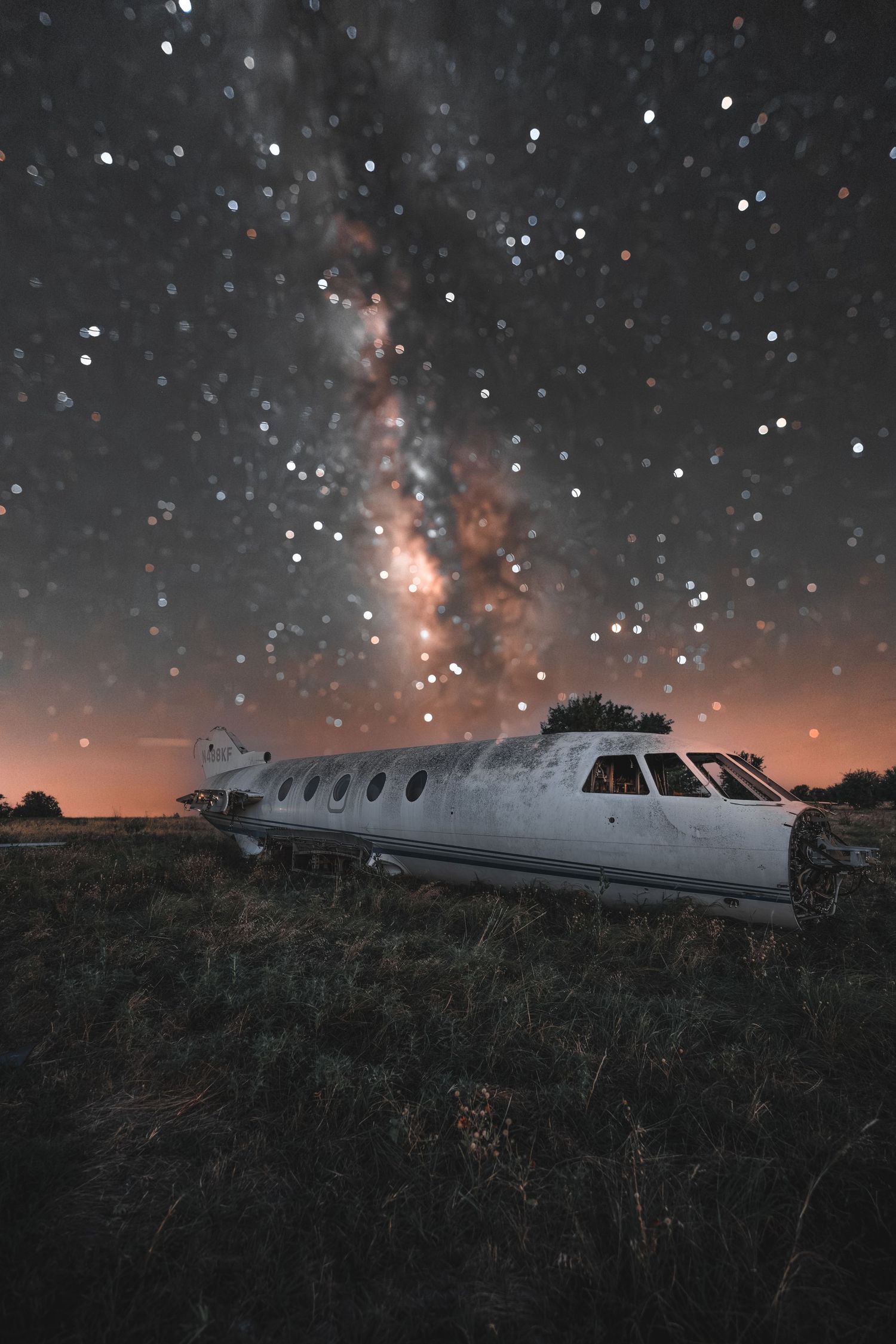 Abandoned airplane fuselage in a field under a starry twilight sky.