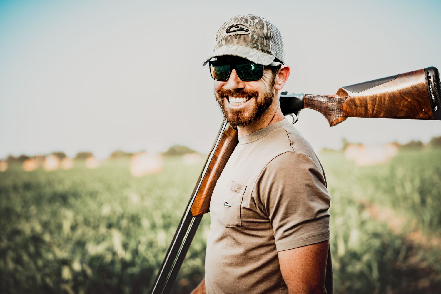 Man in casual attire holding shotgun for clay target shooting against blue sky.
