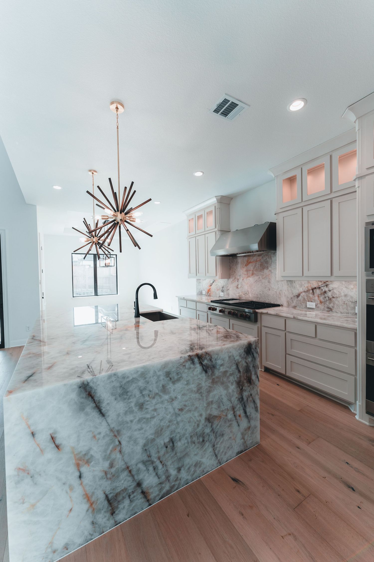 Modern kitchen featuring white cabinetry, starburst chandelier, and dramatic marble waterfall island.