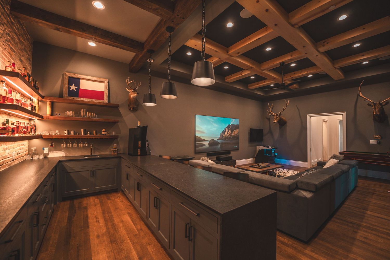 Rustic home bar with wooden coffered ceiling, Texas flag, and ambient lighting.