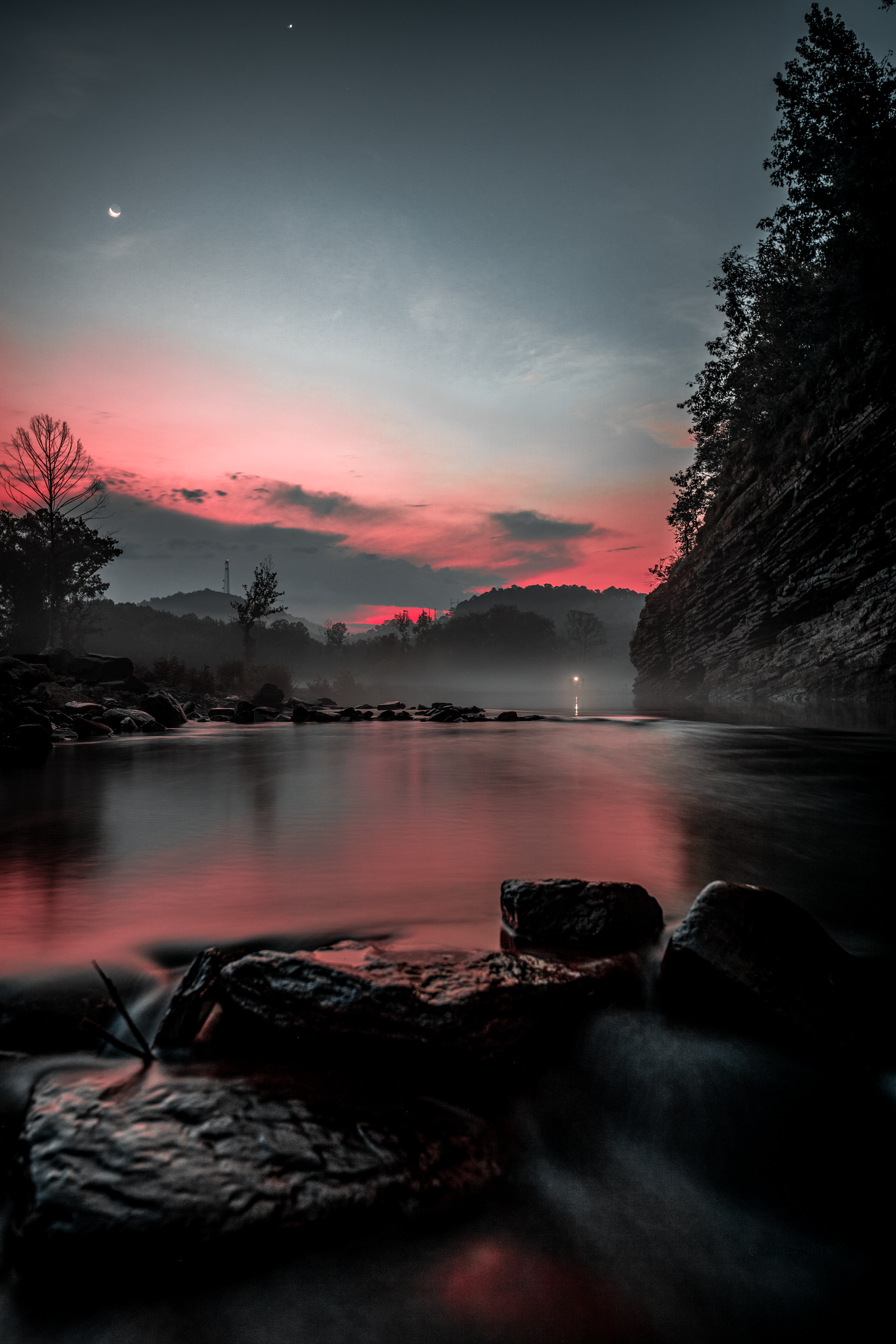 A serene lake reflects pink sunset skies while rocks dot the misty shoreline.